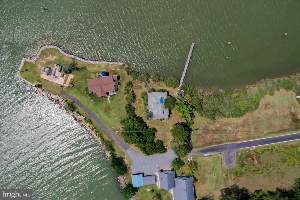 Waterfront property with a long dock, shoreline riprap, and a blue rectangular pool or water feature.
