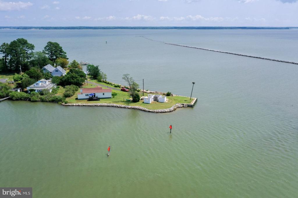 Aerial view of waterfront homes on a rock-lined peninsula with a dock and calm surrounding water.