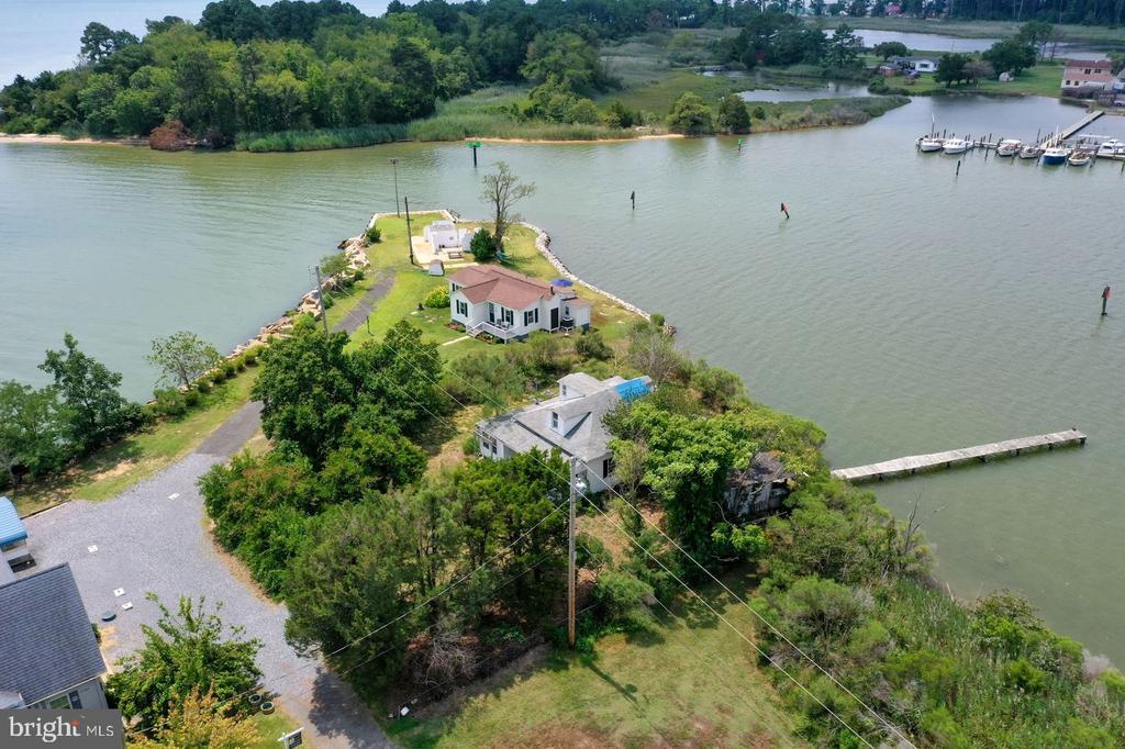 Aerial view of a waterfront home on a tree-lined point, with a long pier extending into the inlet.