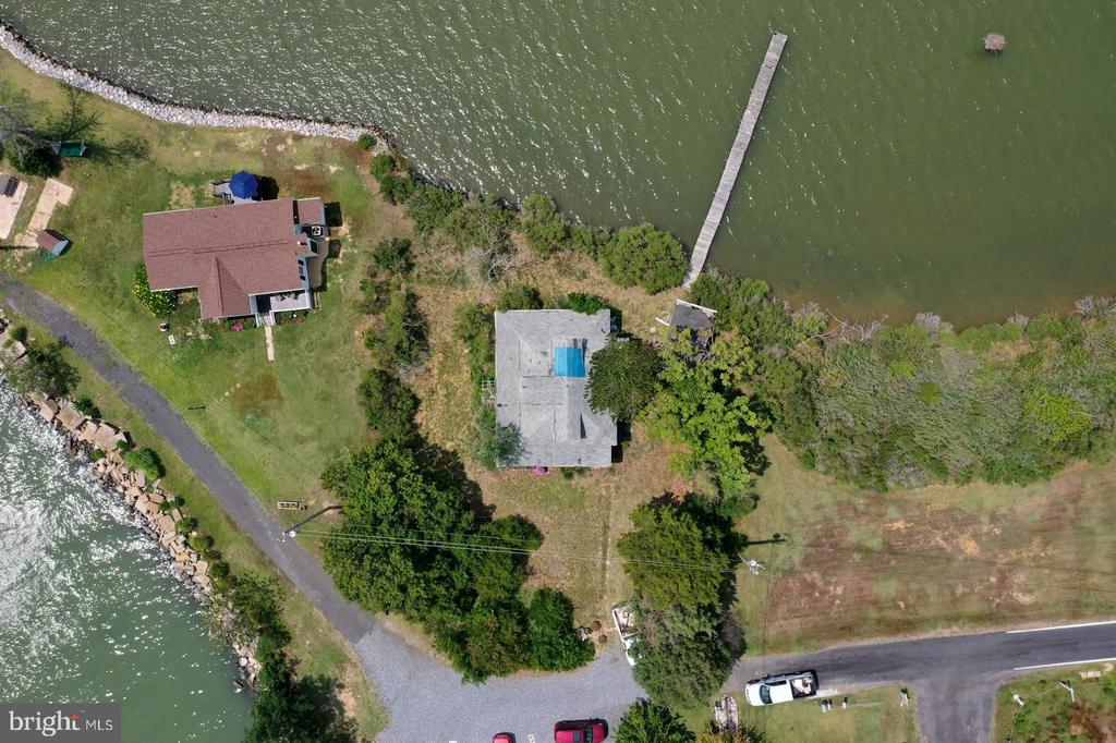 Aerial view of two waterfront homes, with a long pier and rocky shoreline.