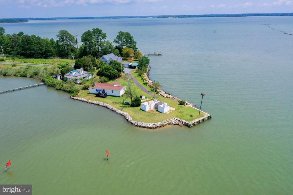 Aerial view of a waterfront point with buildings, a rock-lined shore, and a dock.