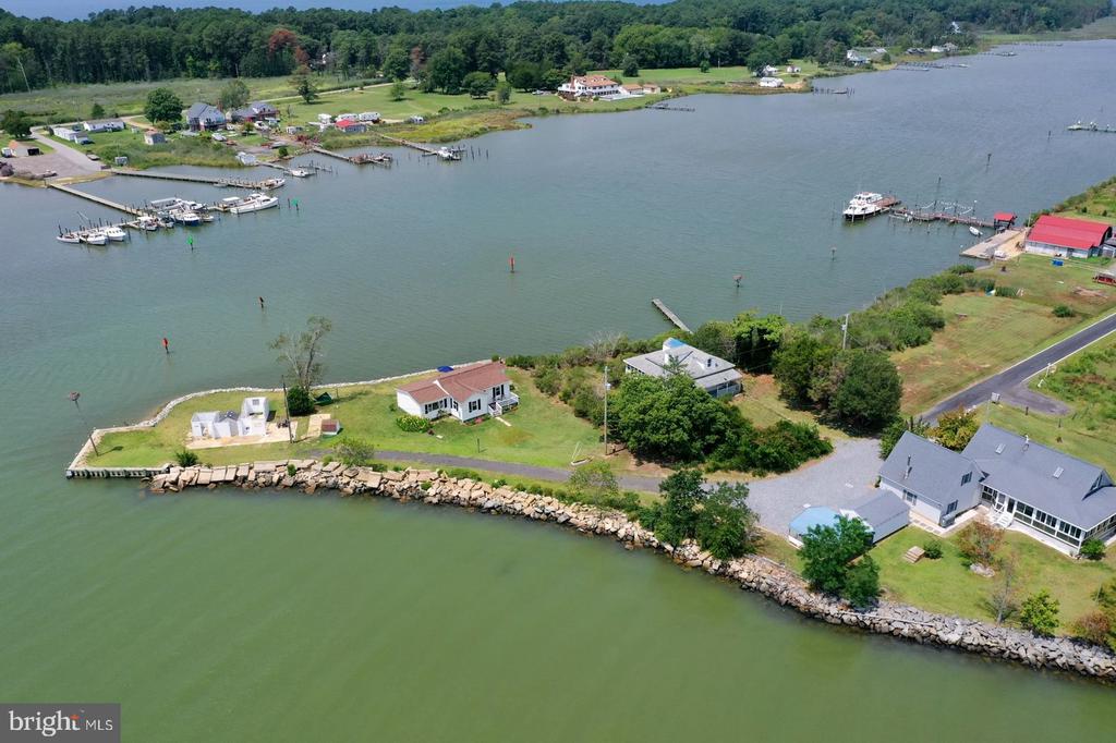 Aerial view of a waterfront home with a rocky shoreline, lawn, and broad inlet.