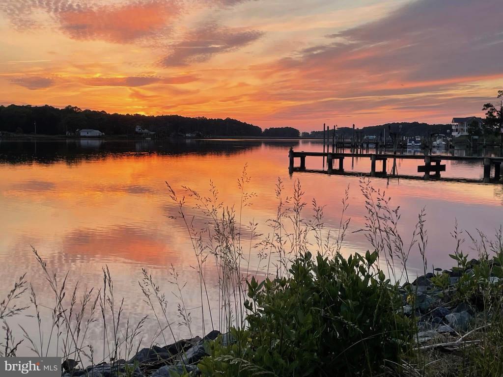 Waterfront at sunset with orange-pink reflections, docks, and shoreline grasses.