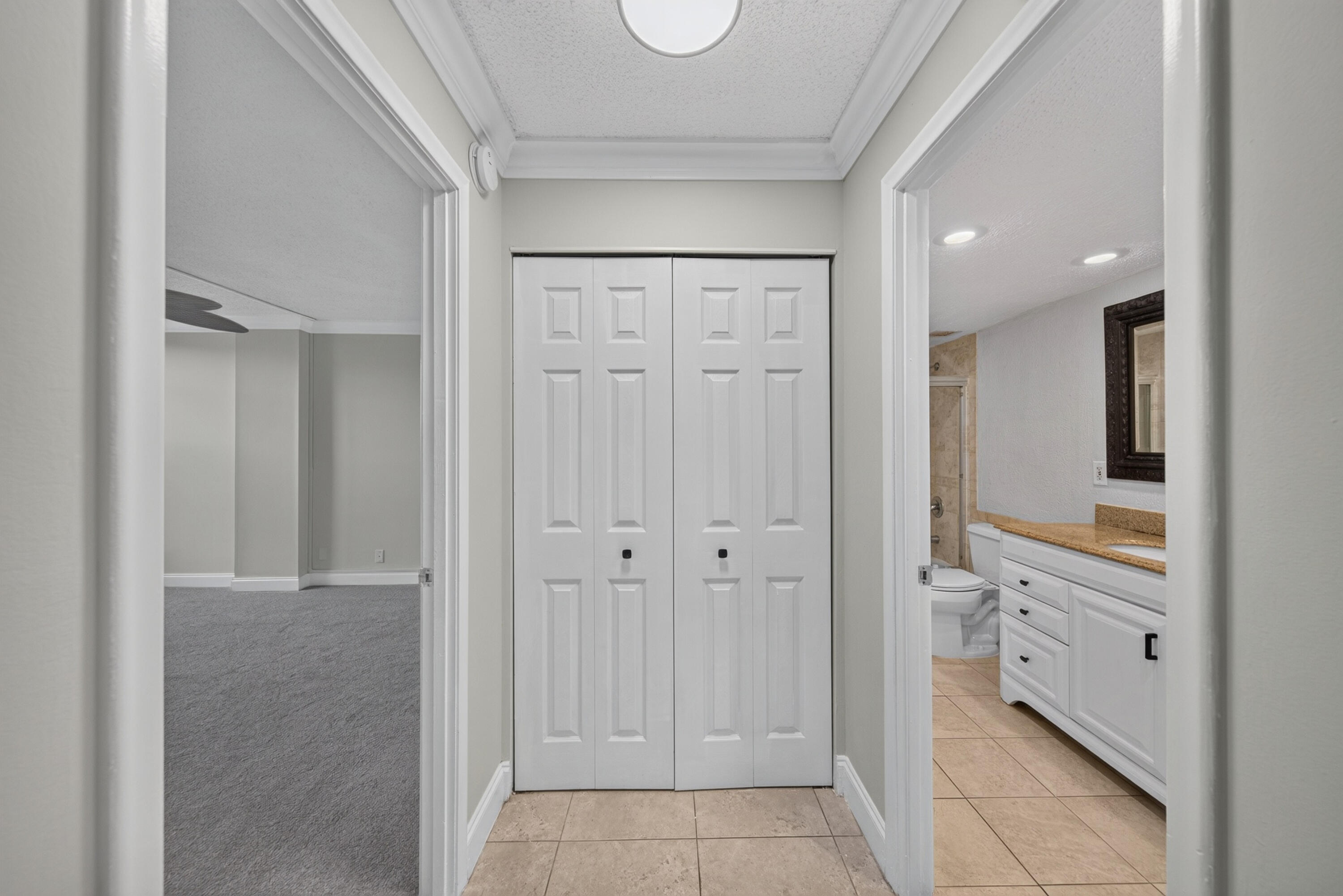 Hallway with white closet doors, opening onto a carpeted room and tiled bathroom.