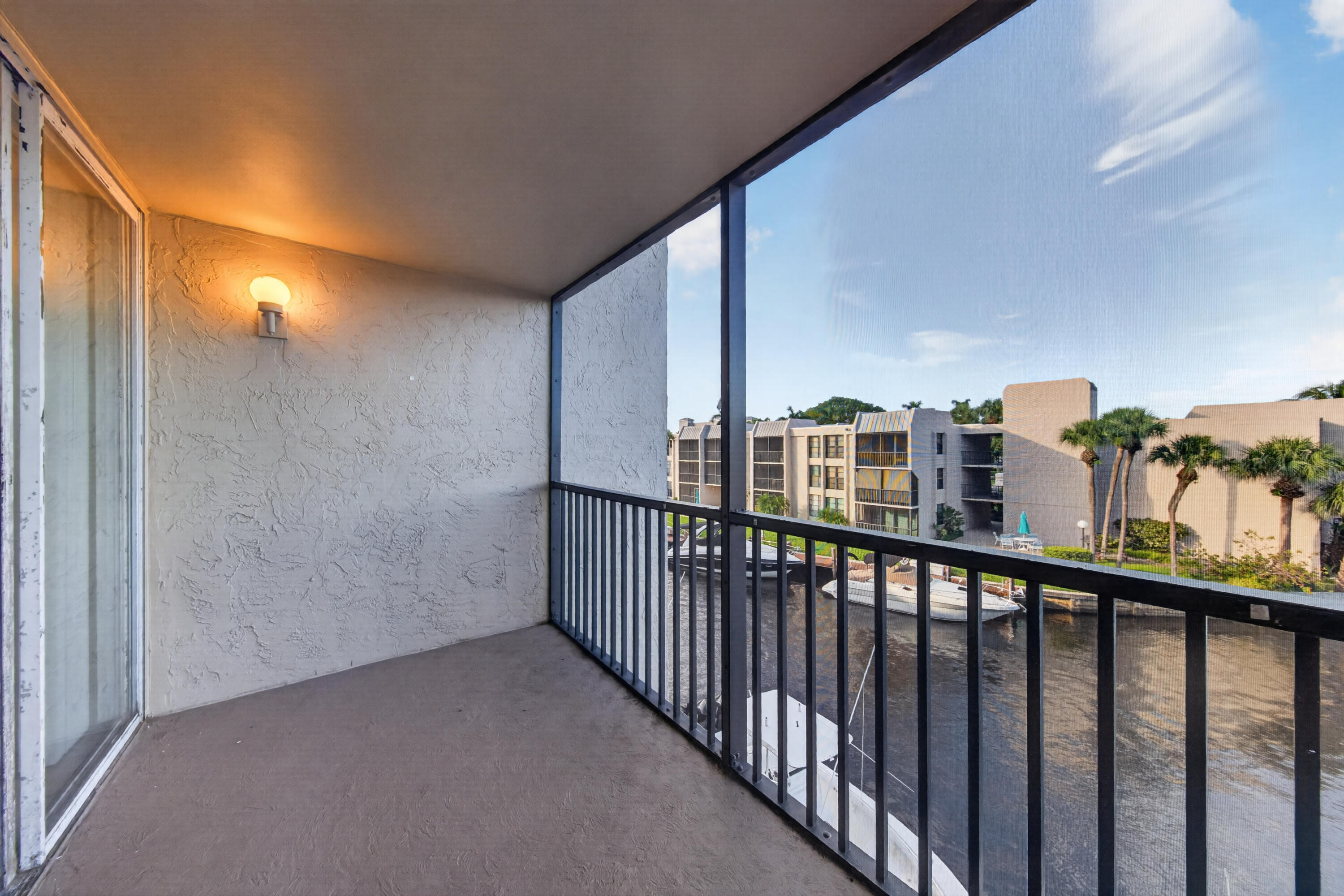 Covered balcony overlooking a canal, boats, palm trees, and neighboring condominiums.