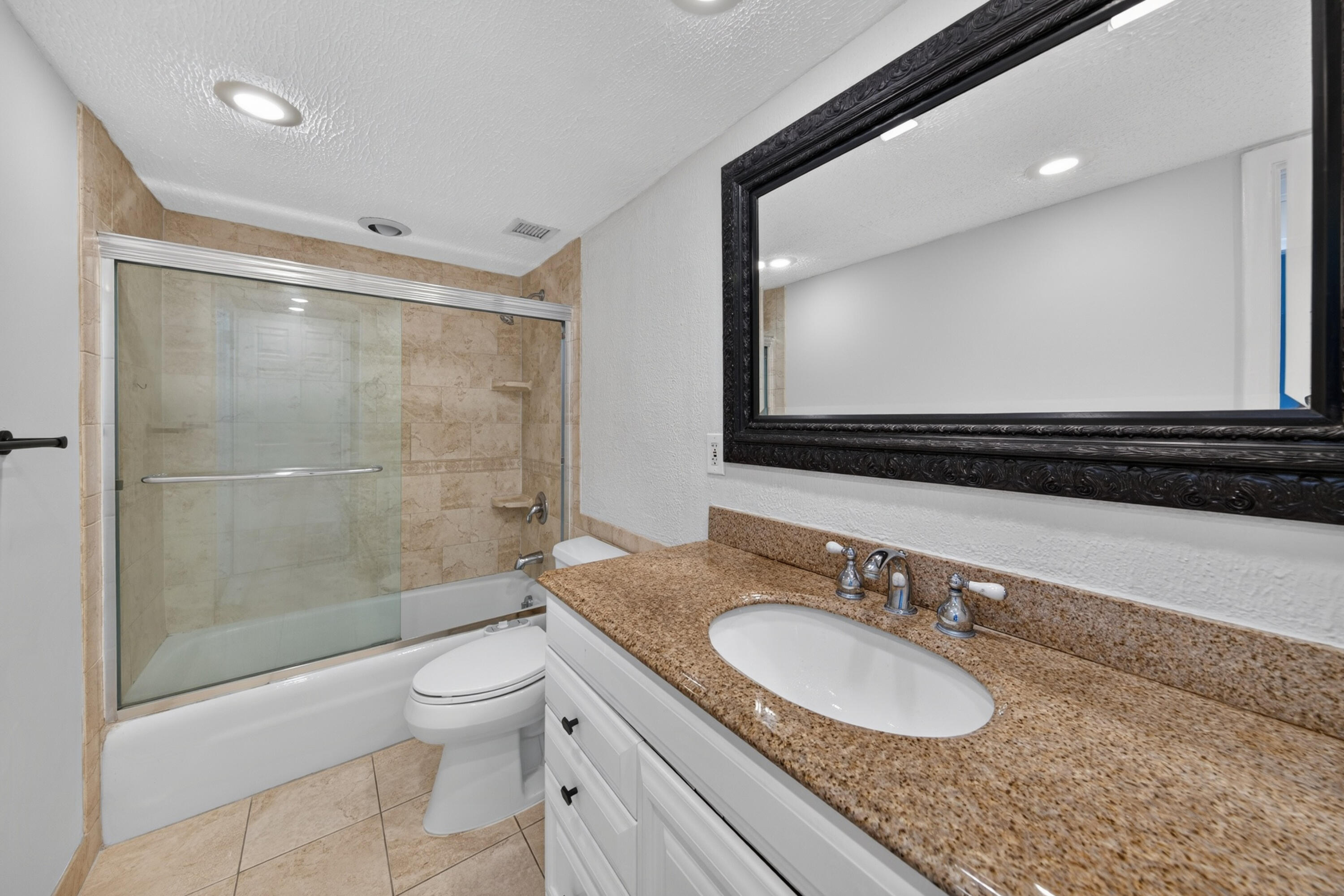 Bathroom with a glass-enclosed tub and shower, granite vanity, and large framed mirror.