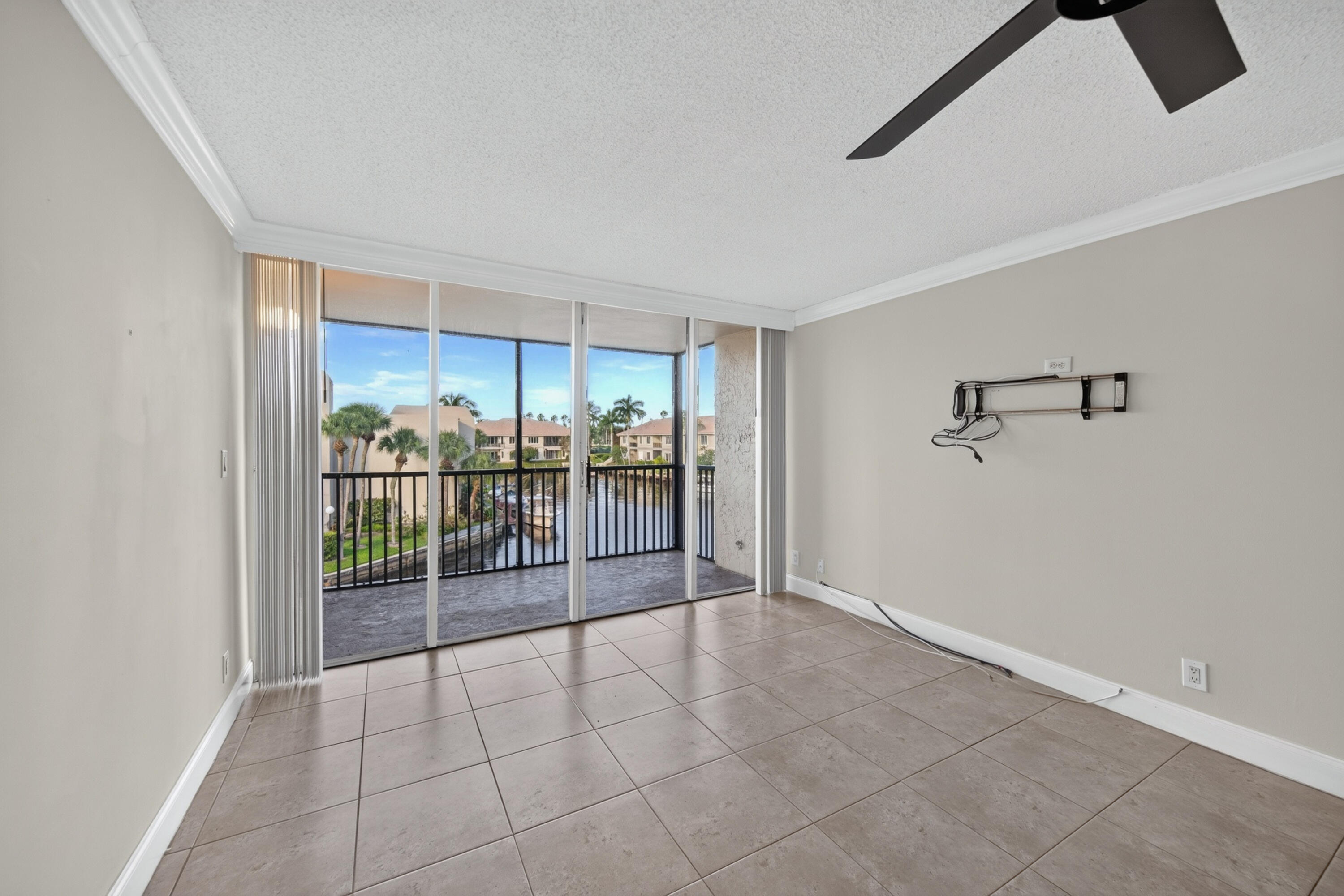Empty tiled room opening to a balcony with canal and palm tree views.