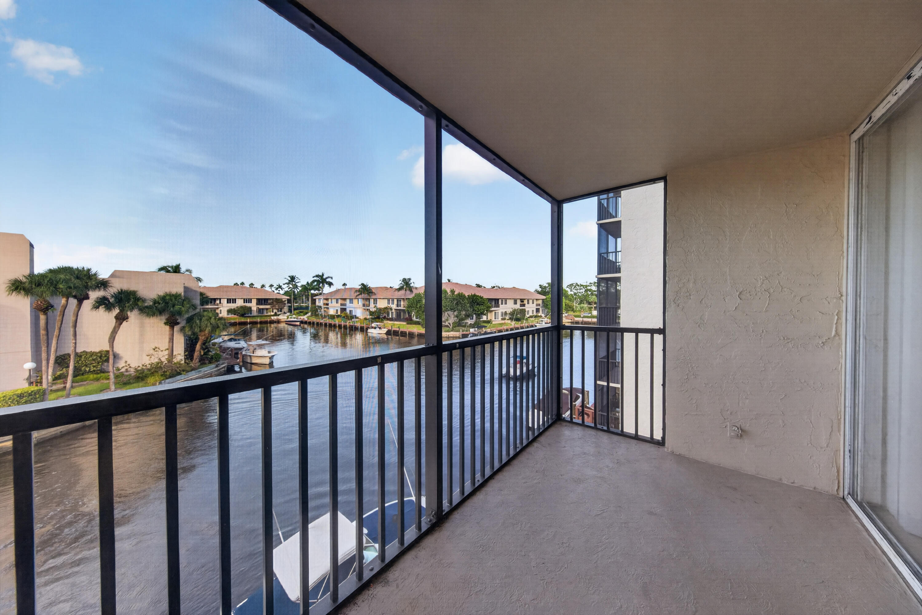 Screened balcony overlooking a canal, with docked boats and palm-lined waterfront buildings.