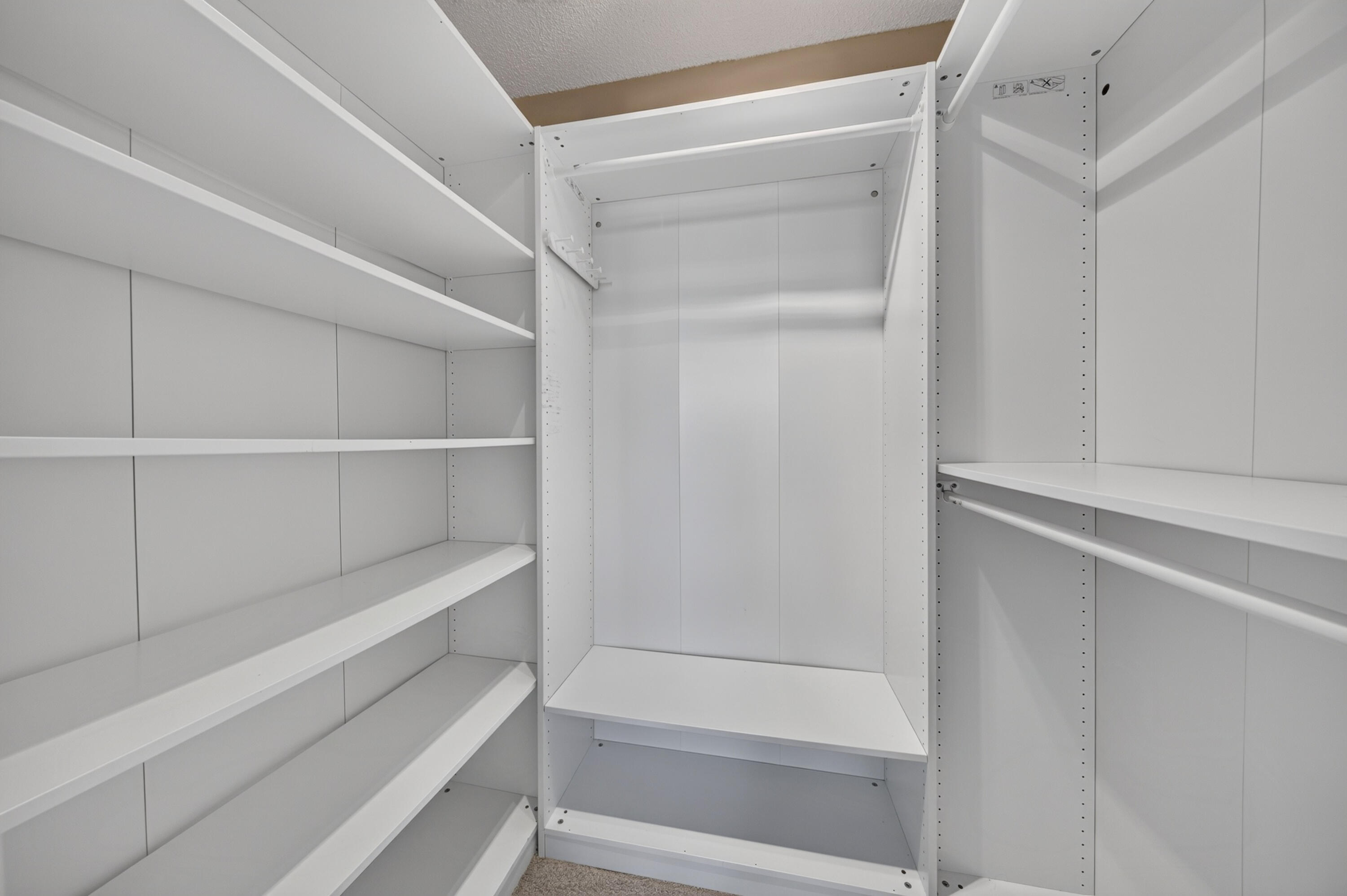 Walk-in closet with white built-in shelves and hanging rails.