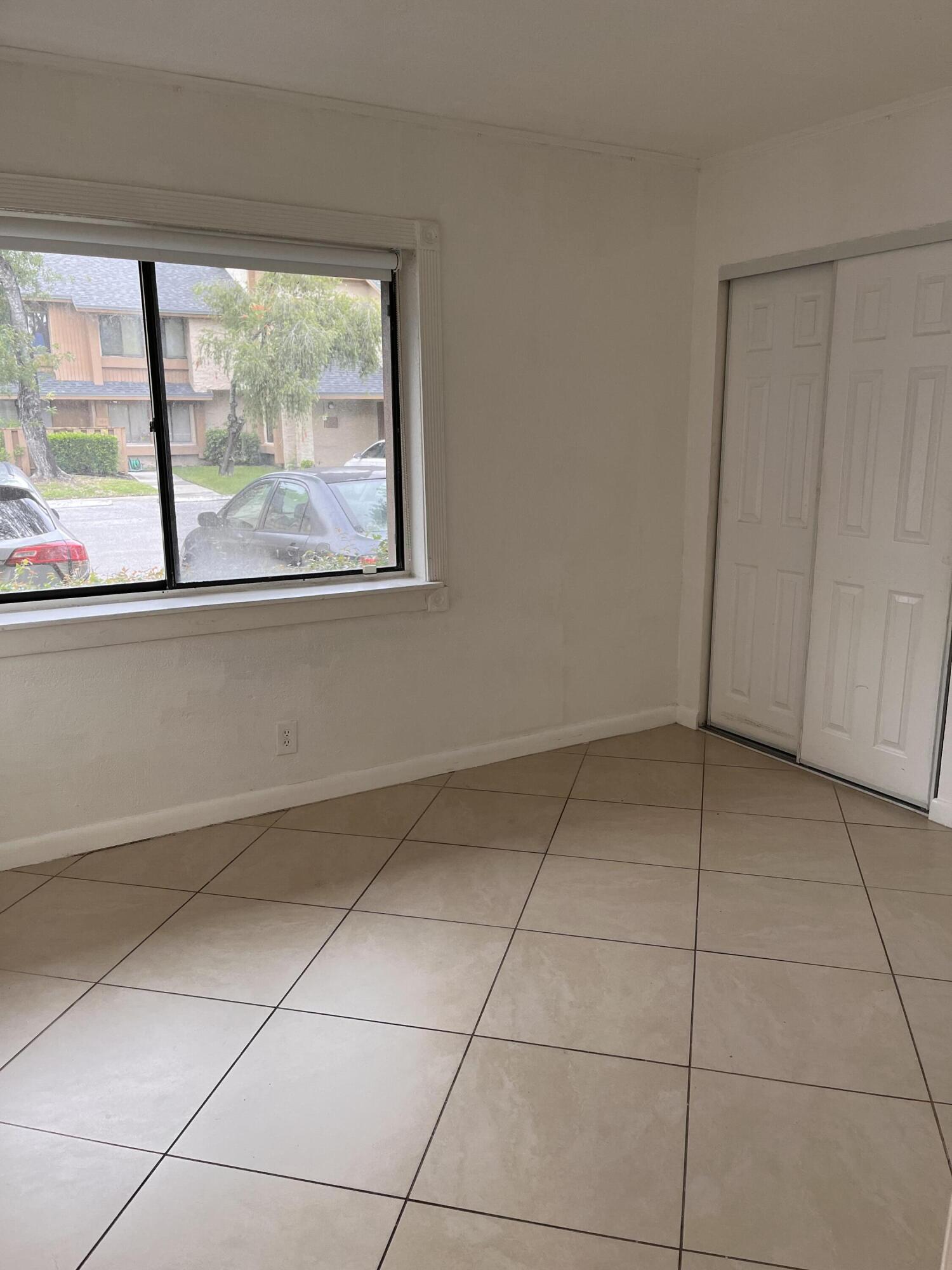 Vacant tiled room with a large window and white sliding closet doors.