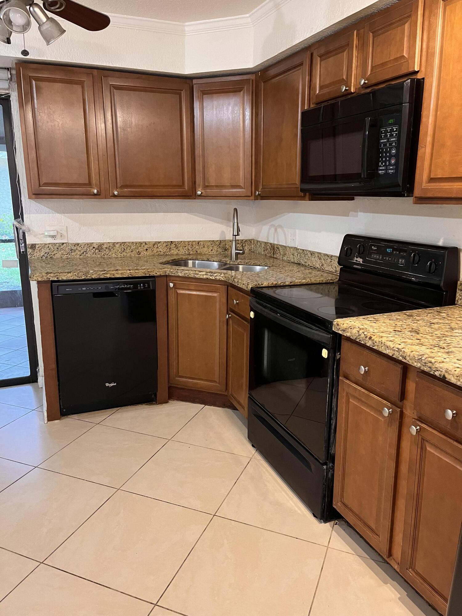 Kitchen with wood cabinets, granite counters, a corner sink, and black appliances.
