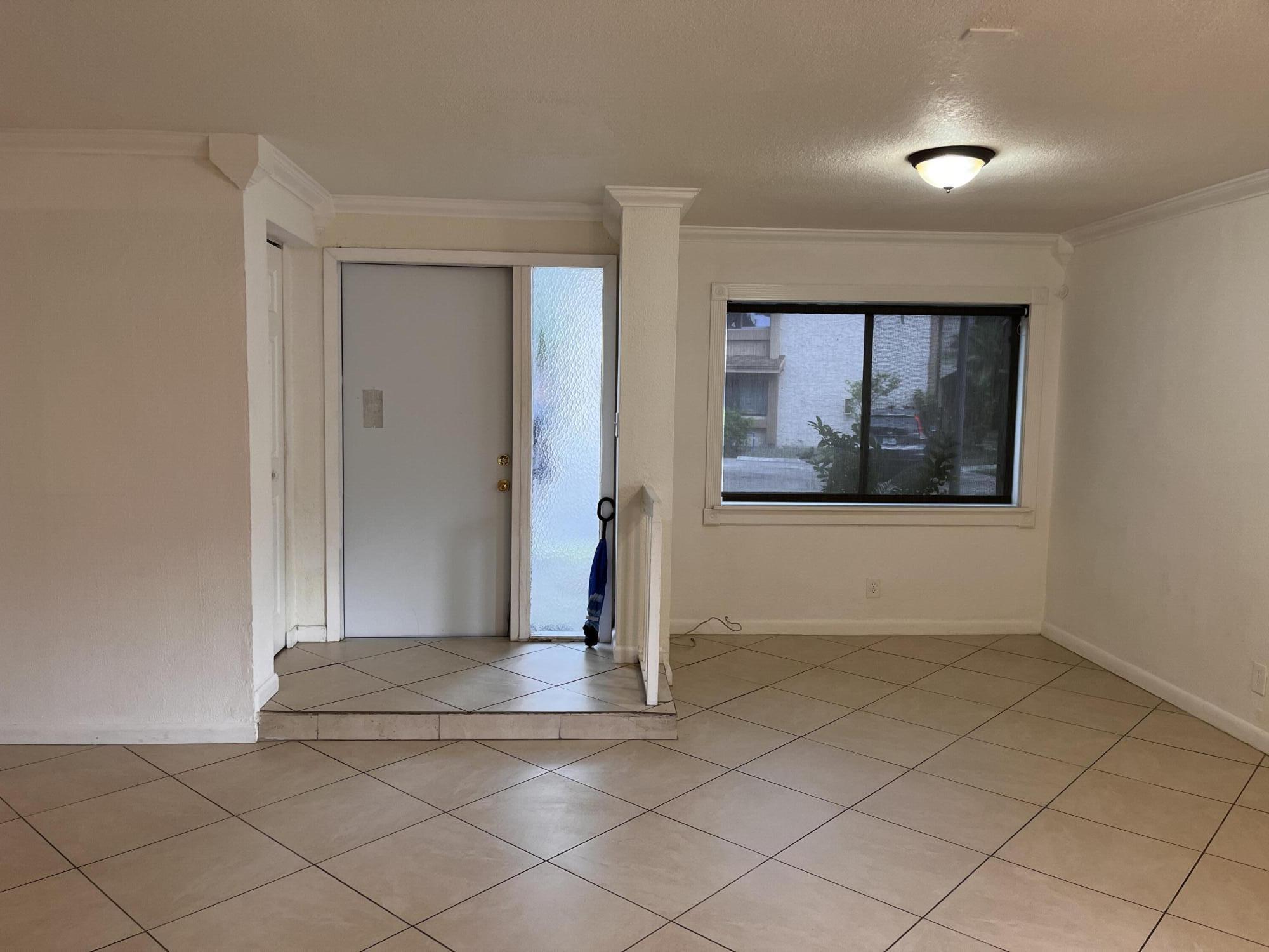 Empty tiled entry area with a white front door, frosted sidelight, and window.