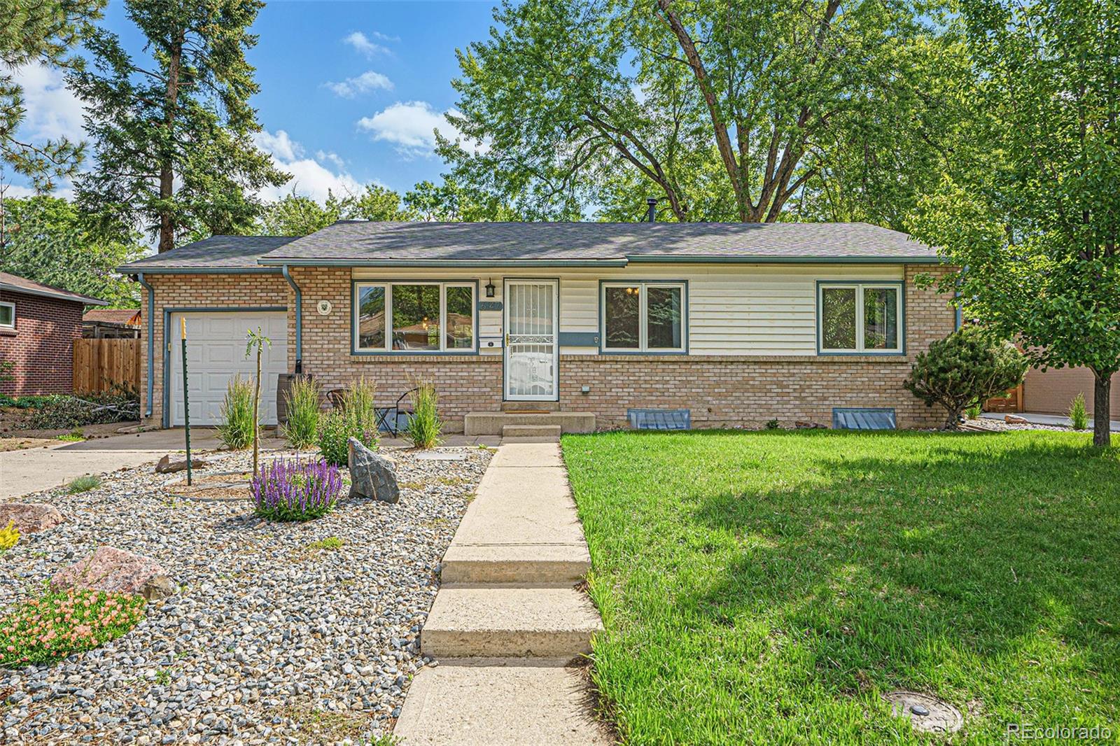 Single-story ranch home with brick exterior, attached garage, stone garden bed, and mature trees.