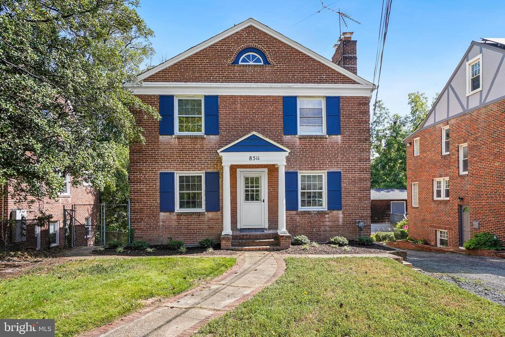 Two-story brick house with blue shutters, a white entry portico, and a curved walkway.