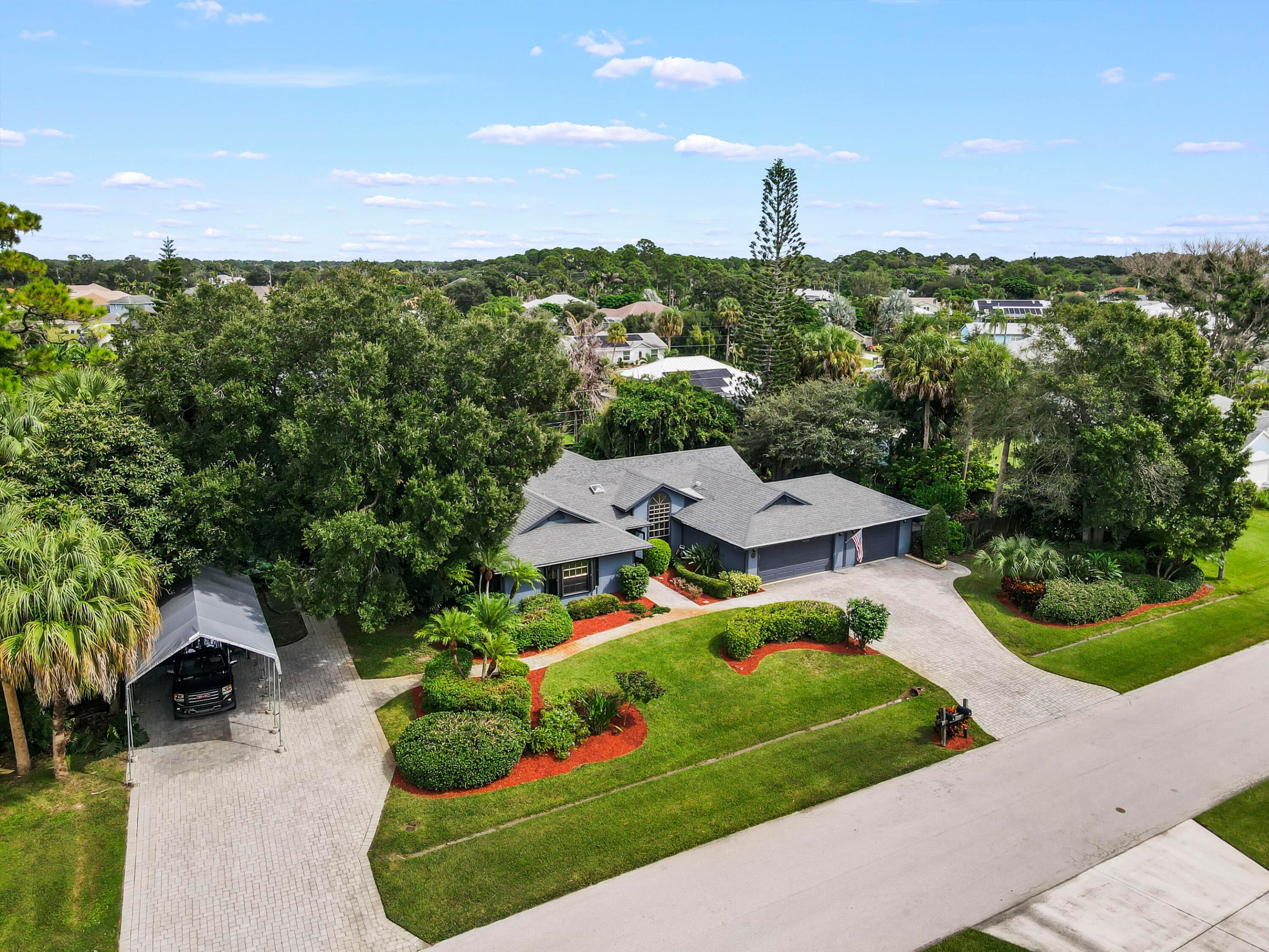 Aerial view of a gray house with a two-car garage, carport, and landscaped yard.