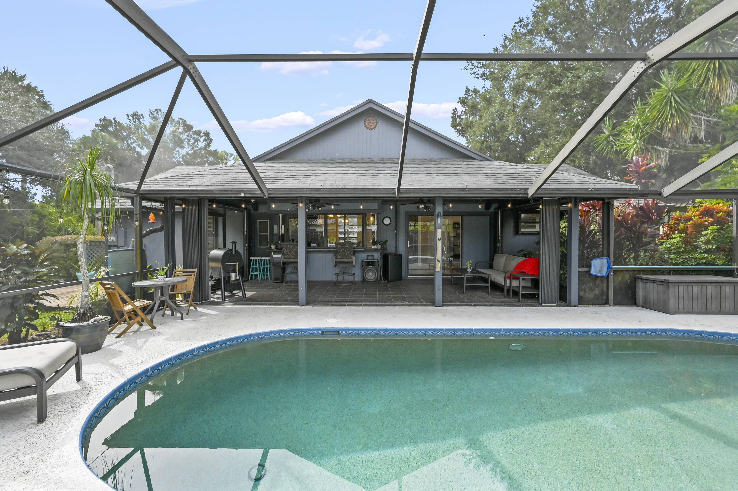 Curved swimming pool beside a screened patio with a bar, grill, and seating.
