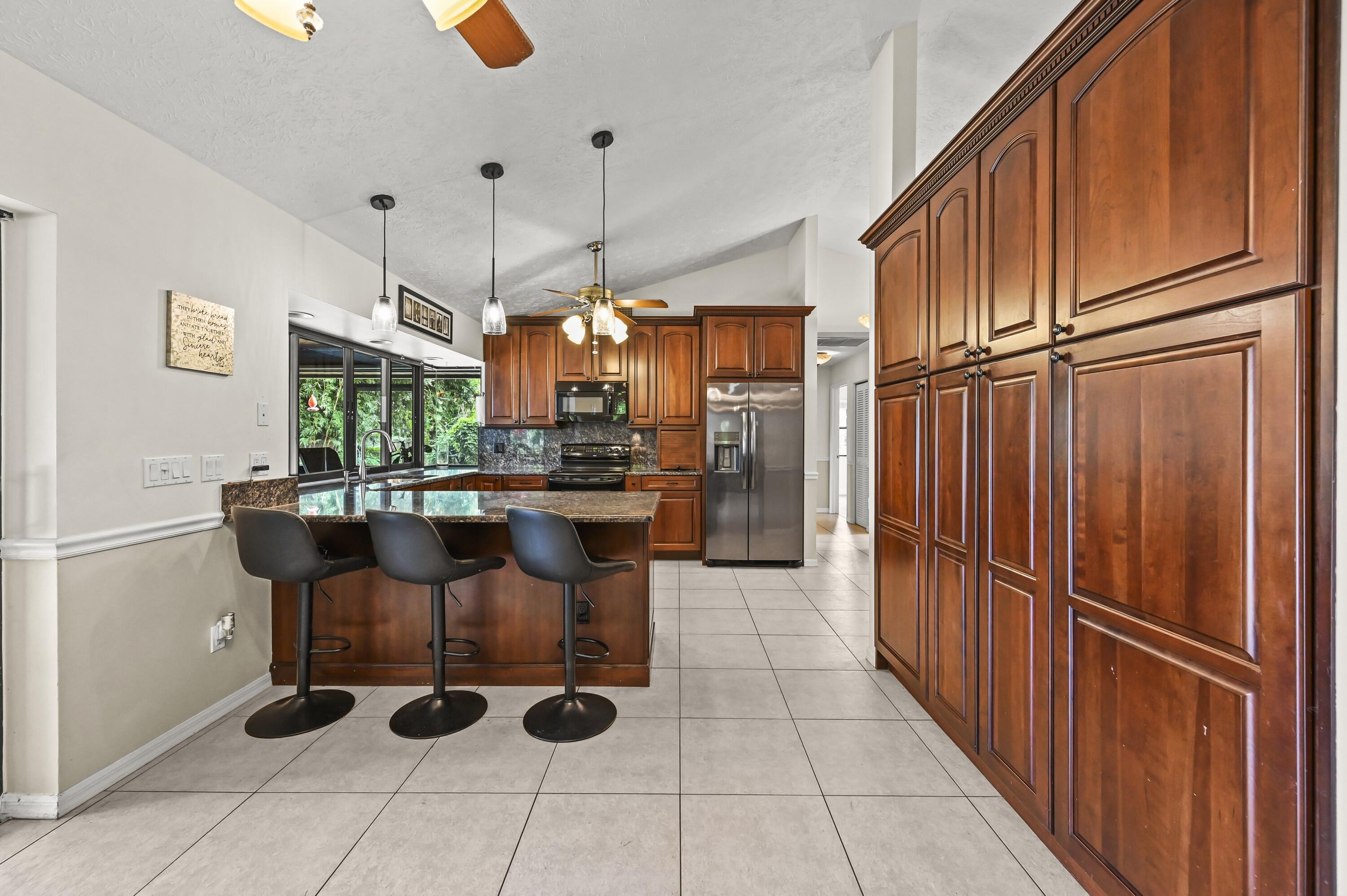 Kitchen with dark wood cabinetry, granite island seating, stainless appliances, and garden-facing windows.