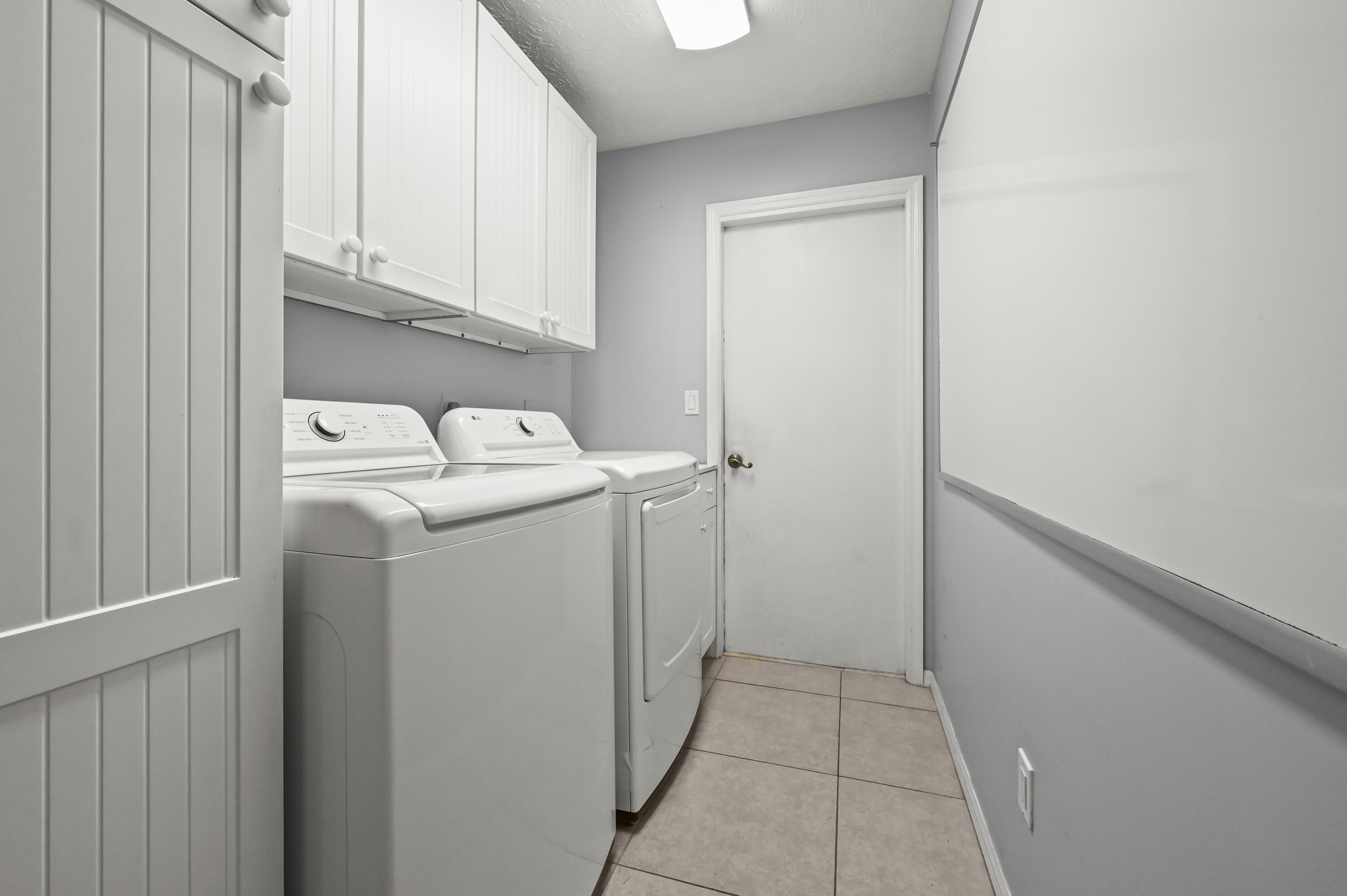Laundry room with a top-loading washer and dryer beneath white cabinets.