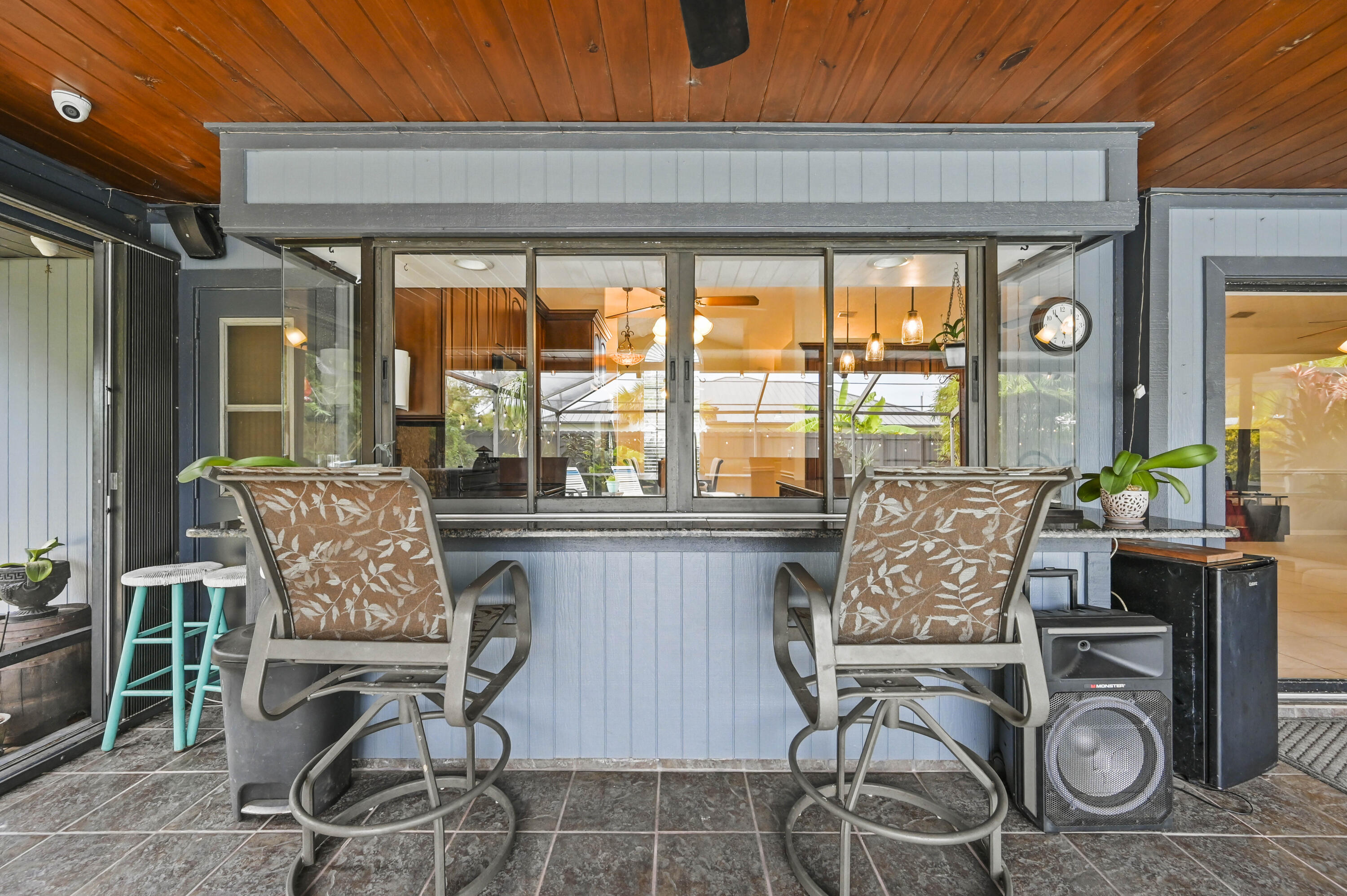 Covered patio bar with two cushioned chairs, turquoise stools, and a pass-through window to the kitchen.