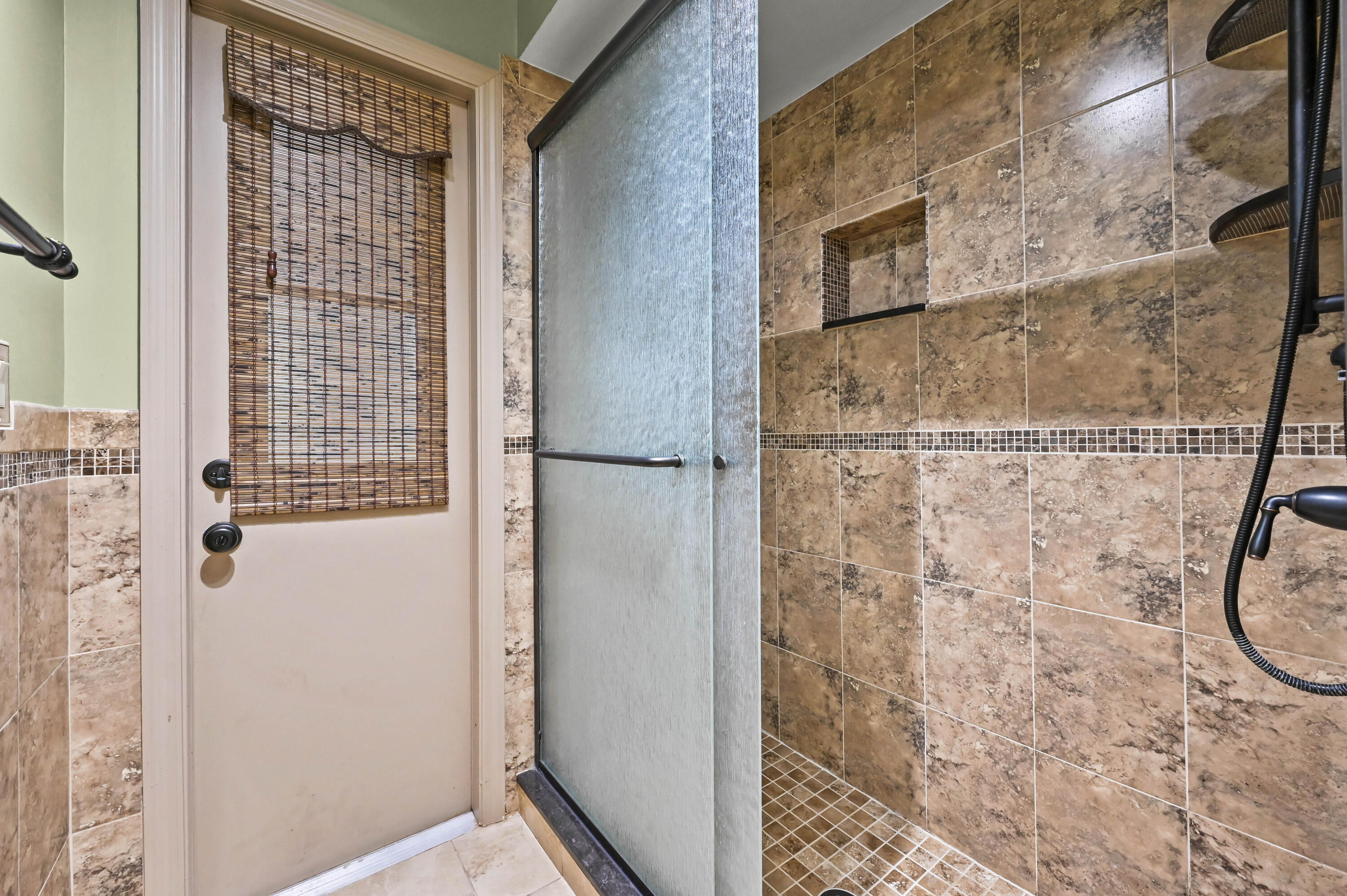Bathroom walk-in shower with frosted glass and brown tiled walls with a built-in niche.