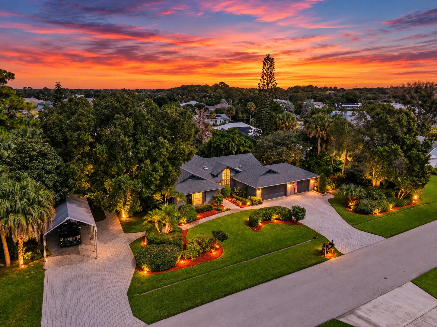 Aerial view of a landscaped single-story home and driveway beneath a vivid sunset.