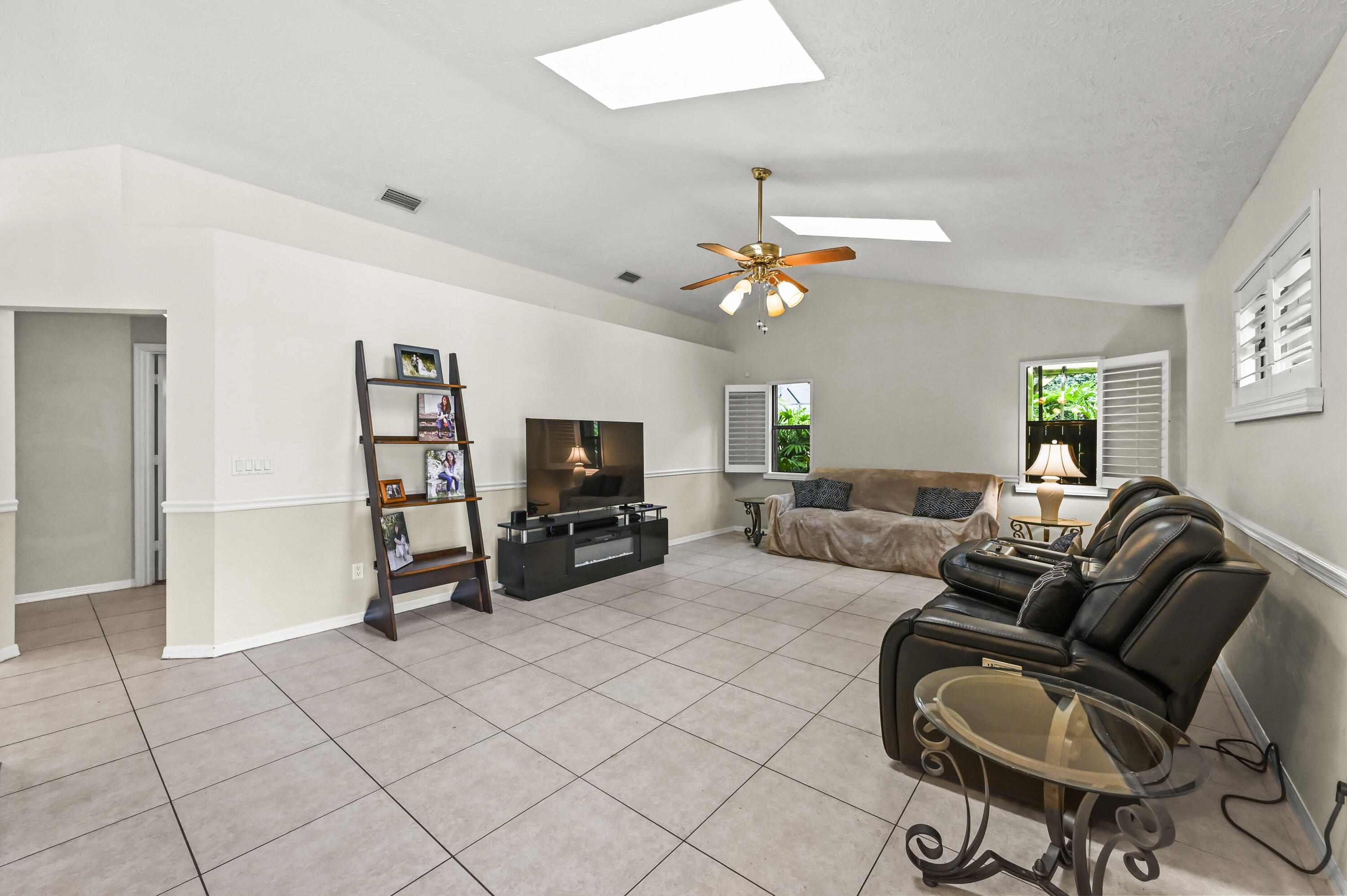 Living room with tiled floors, black leather recliners, and plantation shutters.