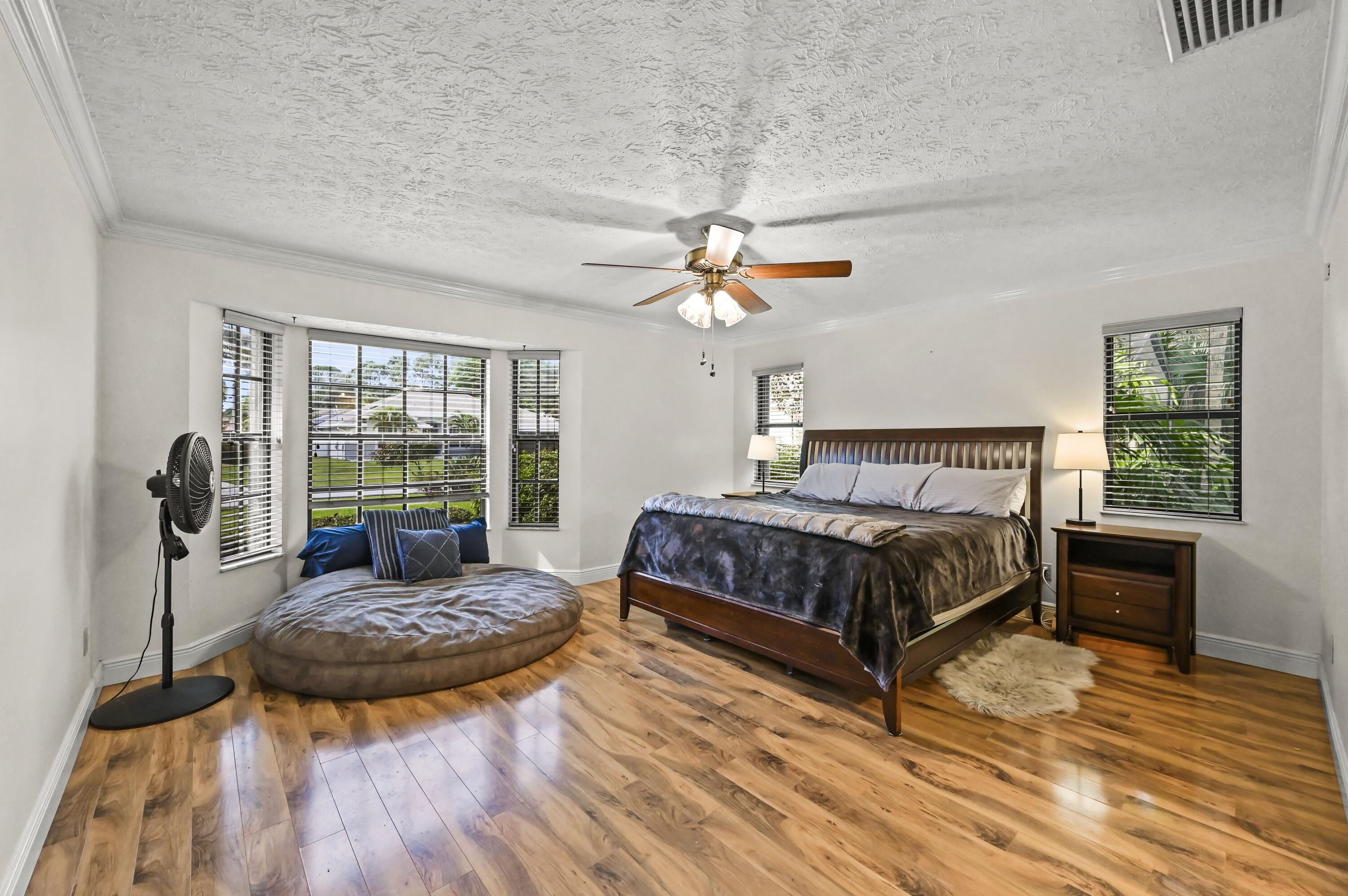 Bedroom with a dark wood bed, round floor cushion, and broad windows overlooking greenery.