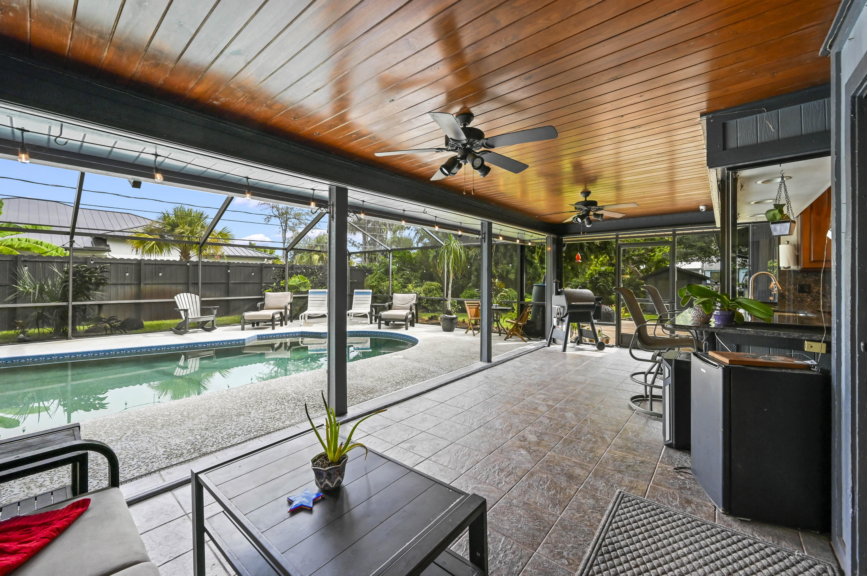 Screened pool patio with a wood-plank ceiling, lounge chairs, and an outdoor kitchen.