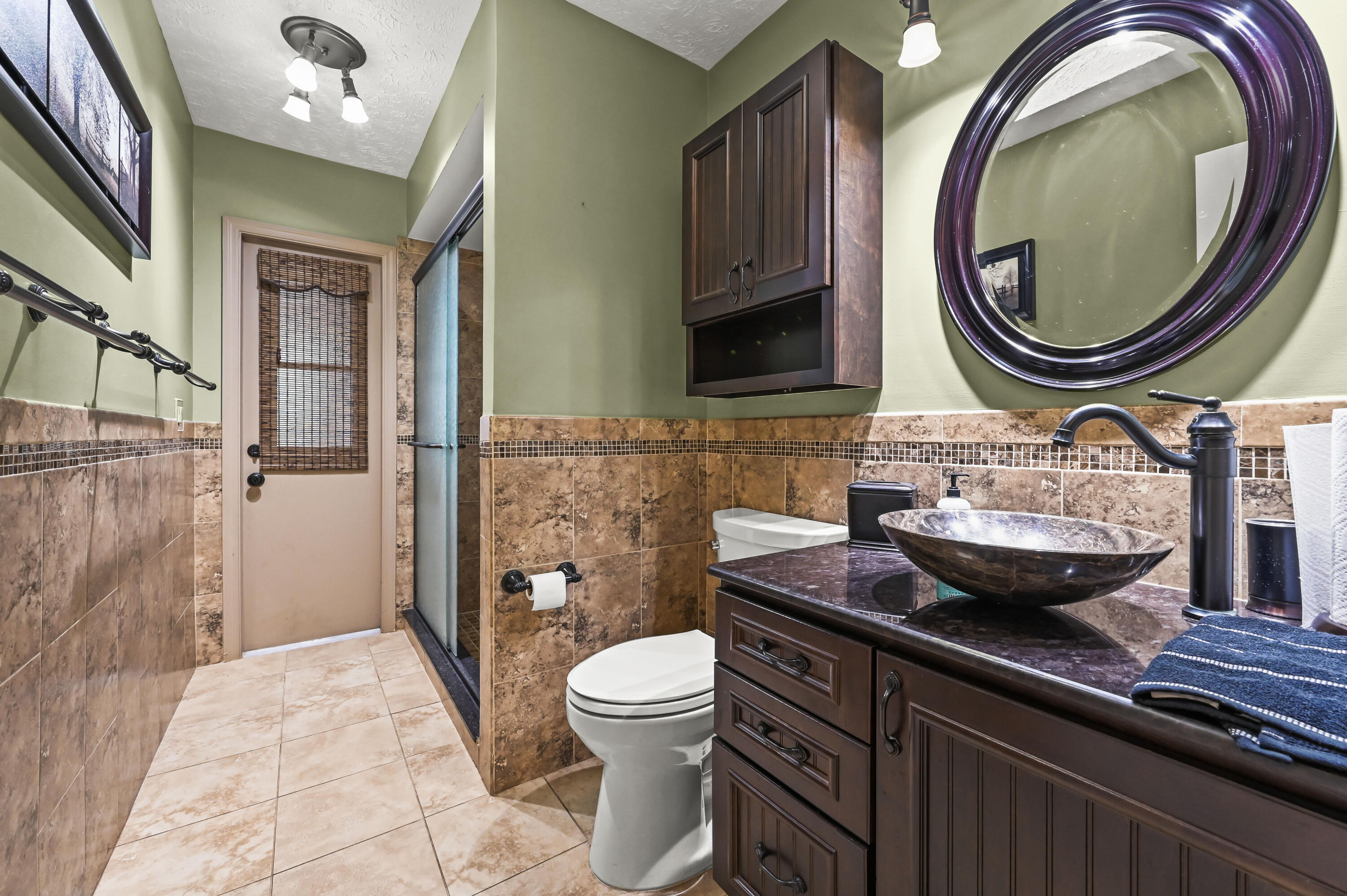 Bathroom with a glass shower, dark wood vanity, vessel sink, and large round mirror.