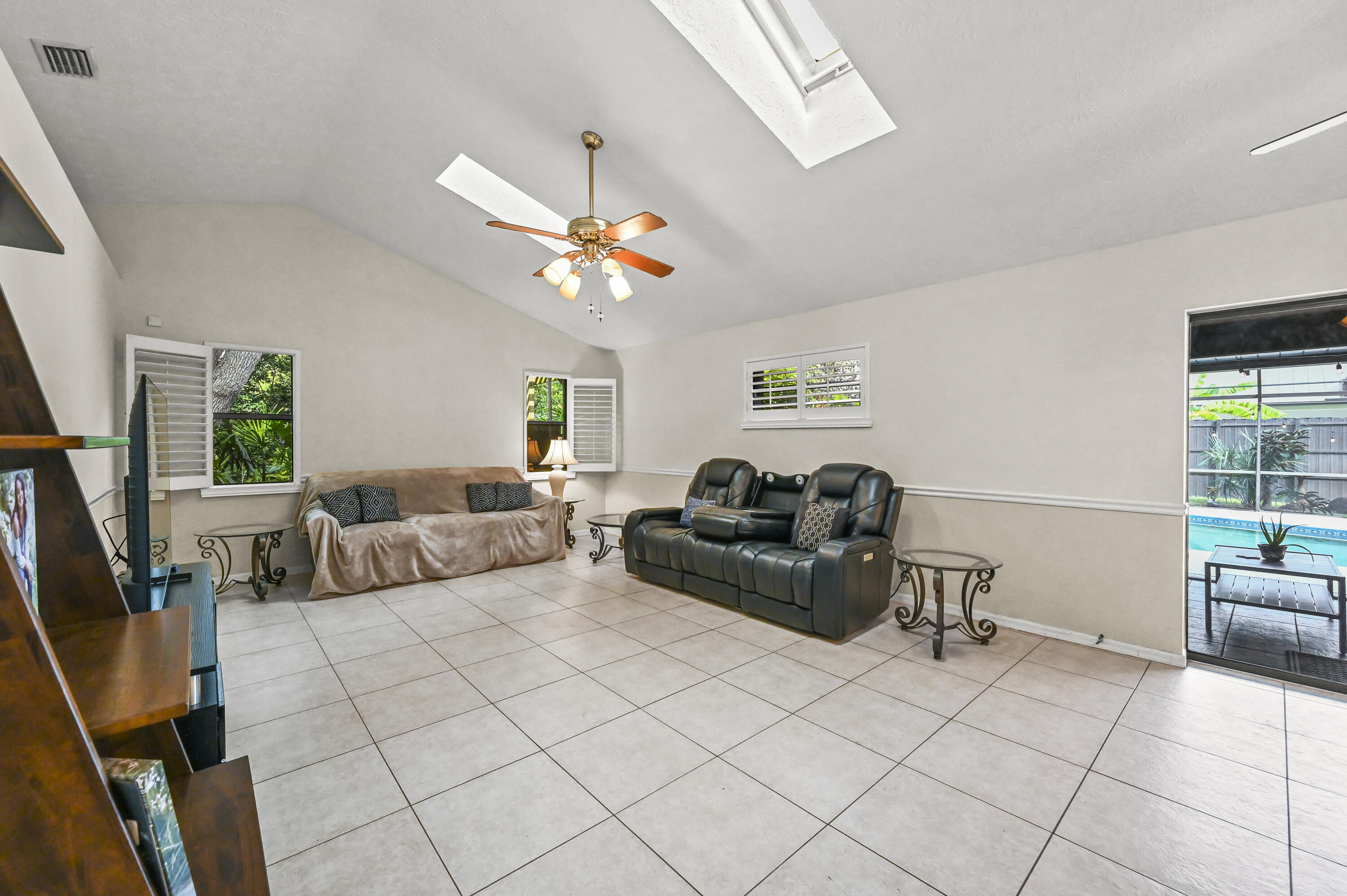 Living room with a vaulted ceiling, tiled floor, and sliding glass door overlooking the pool.