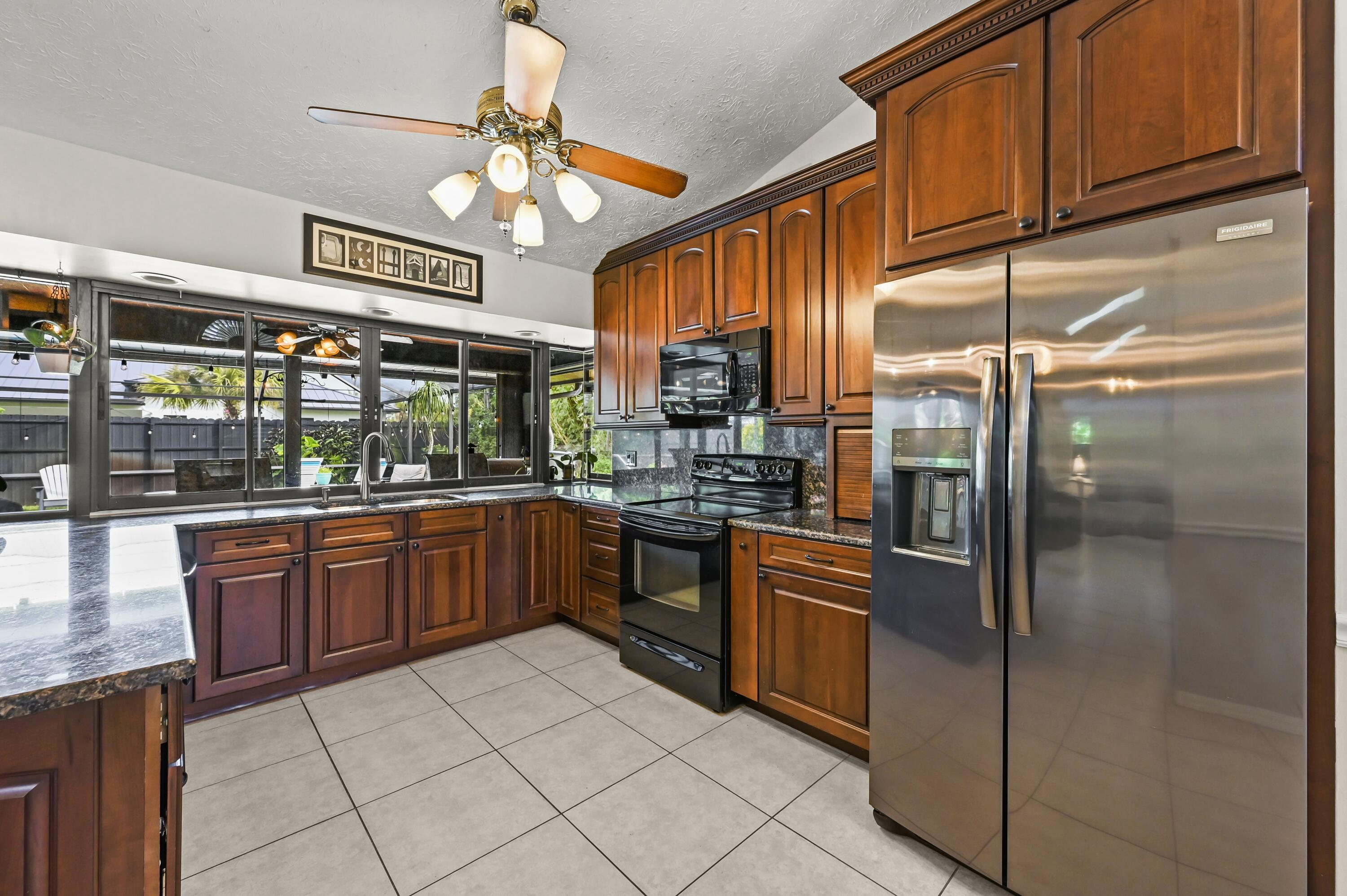 Kitchen with cherry cabinets, granite counters, stainless steel appliances, and large windows overlooking a fenced yard.