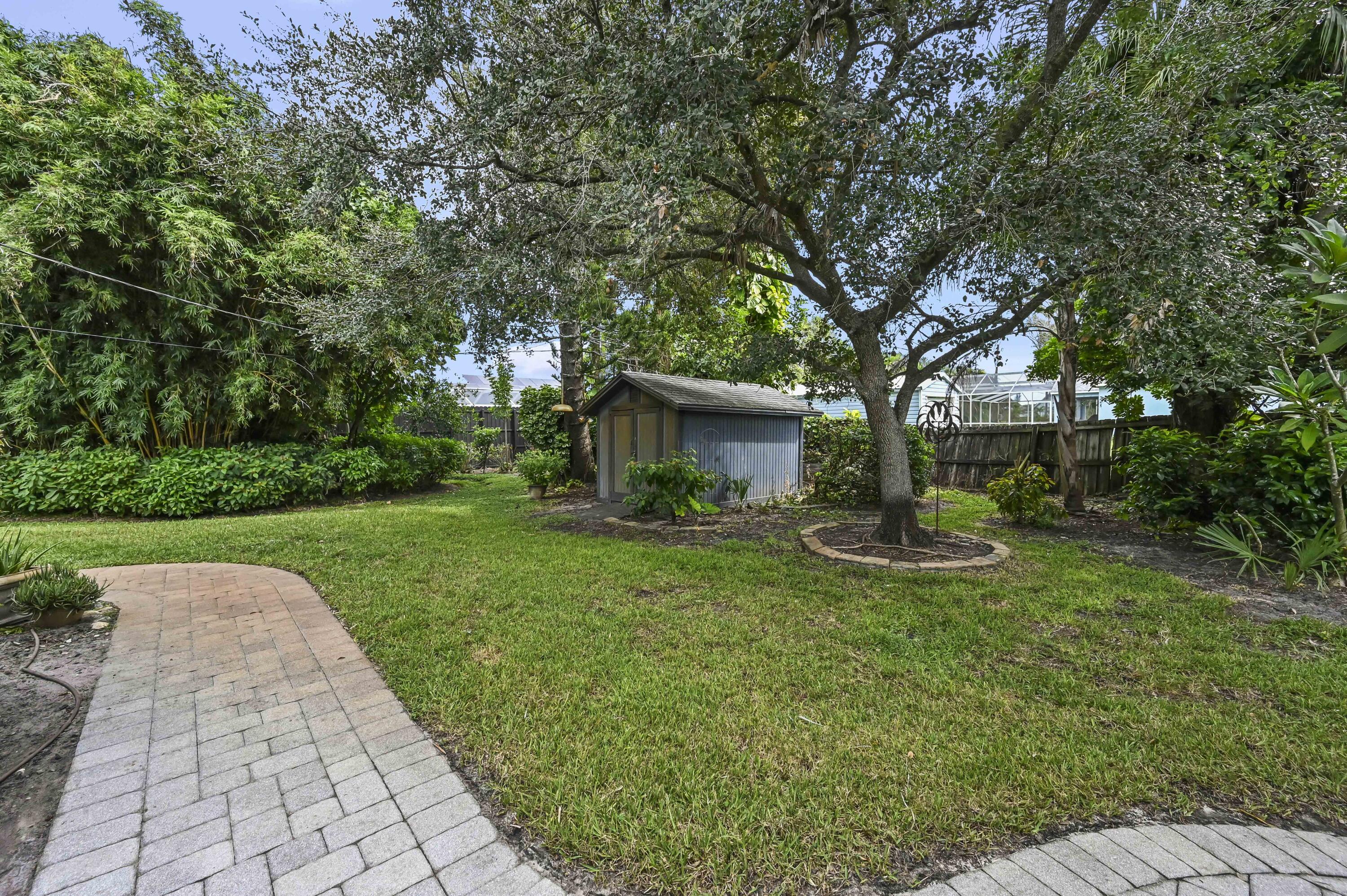 Backyard with a lawn, mature trees, a storage shed, and curved paver paths.