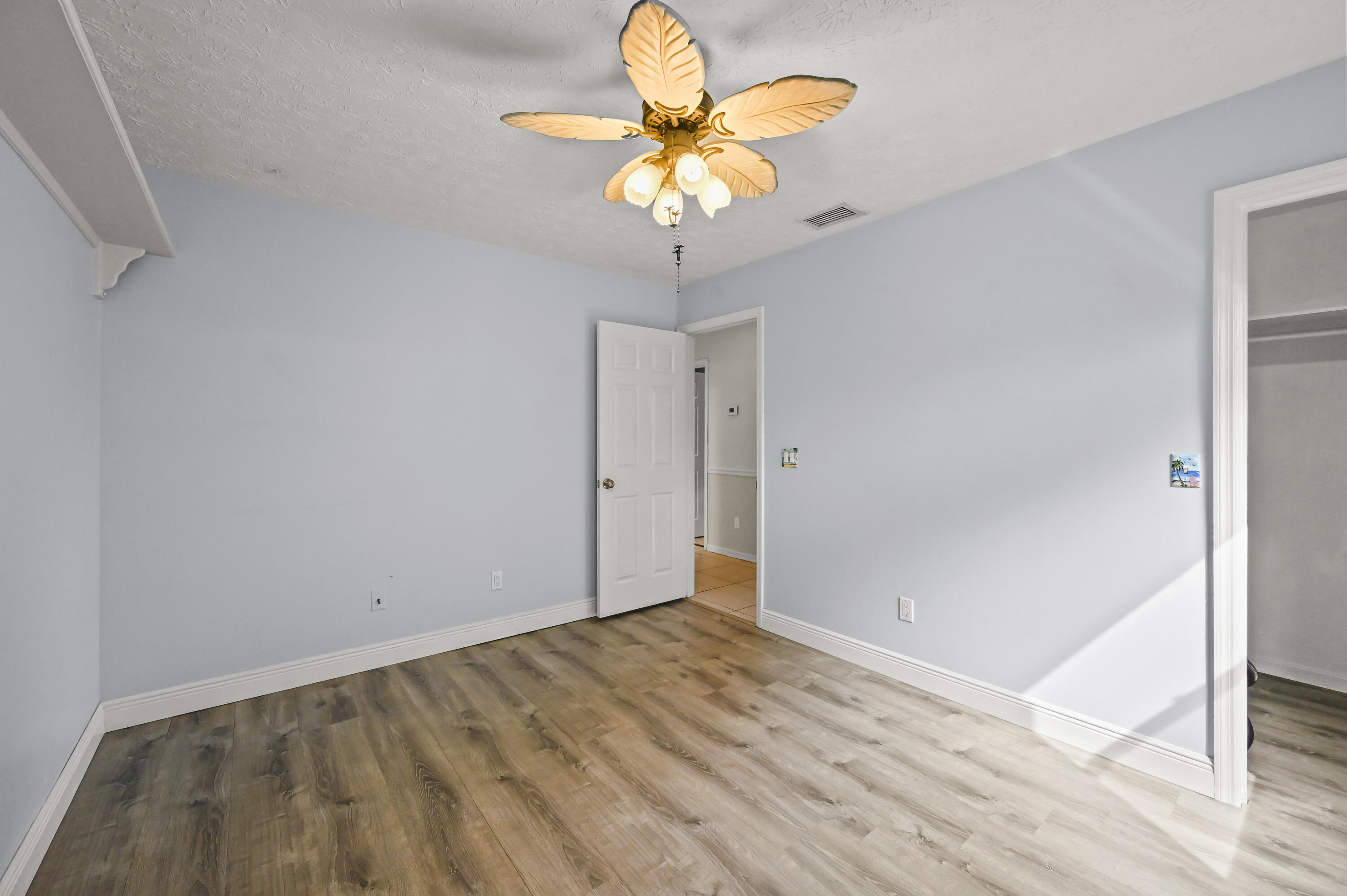 Empty bedroom with wood-look flooring, a decorative ceiling fan, and an open closet doorway.