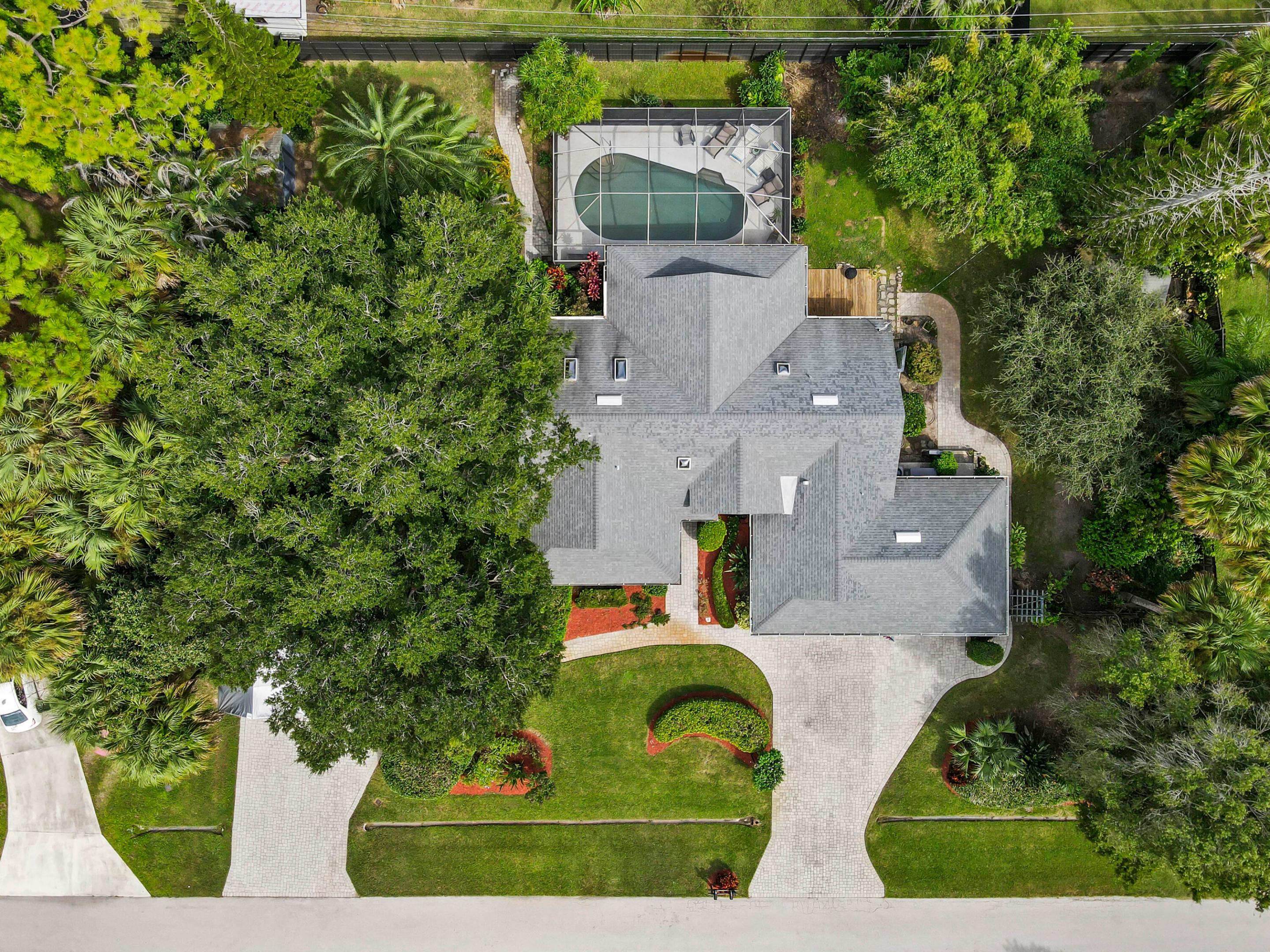 Aerial view of a gray-roofed home and landscaped yard with a screened pool and curved paver paths.