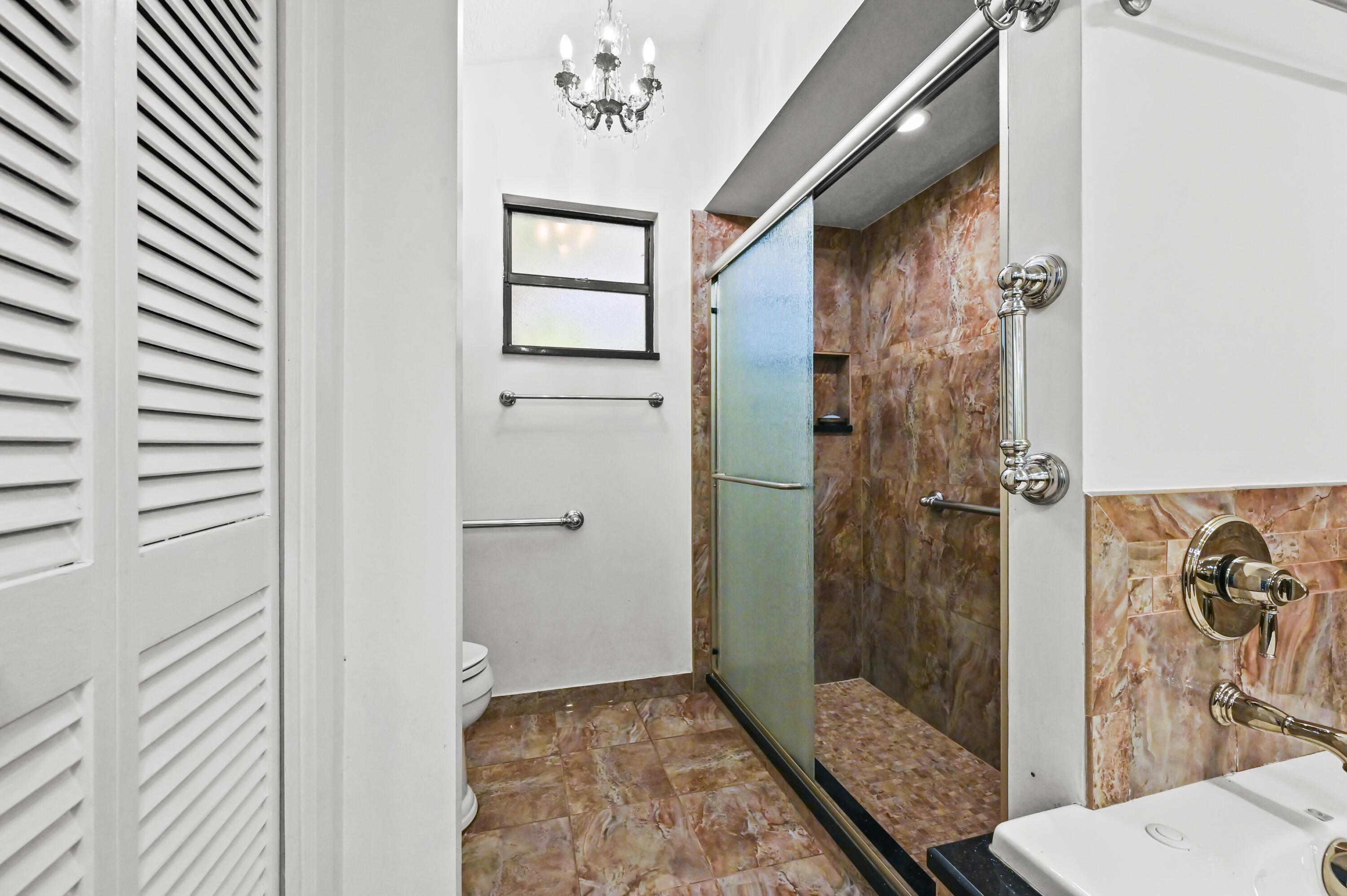Bathroom with a stone-tiled walk-in shower, frosted glass door, and chandelier.