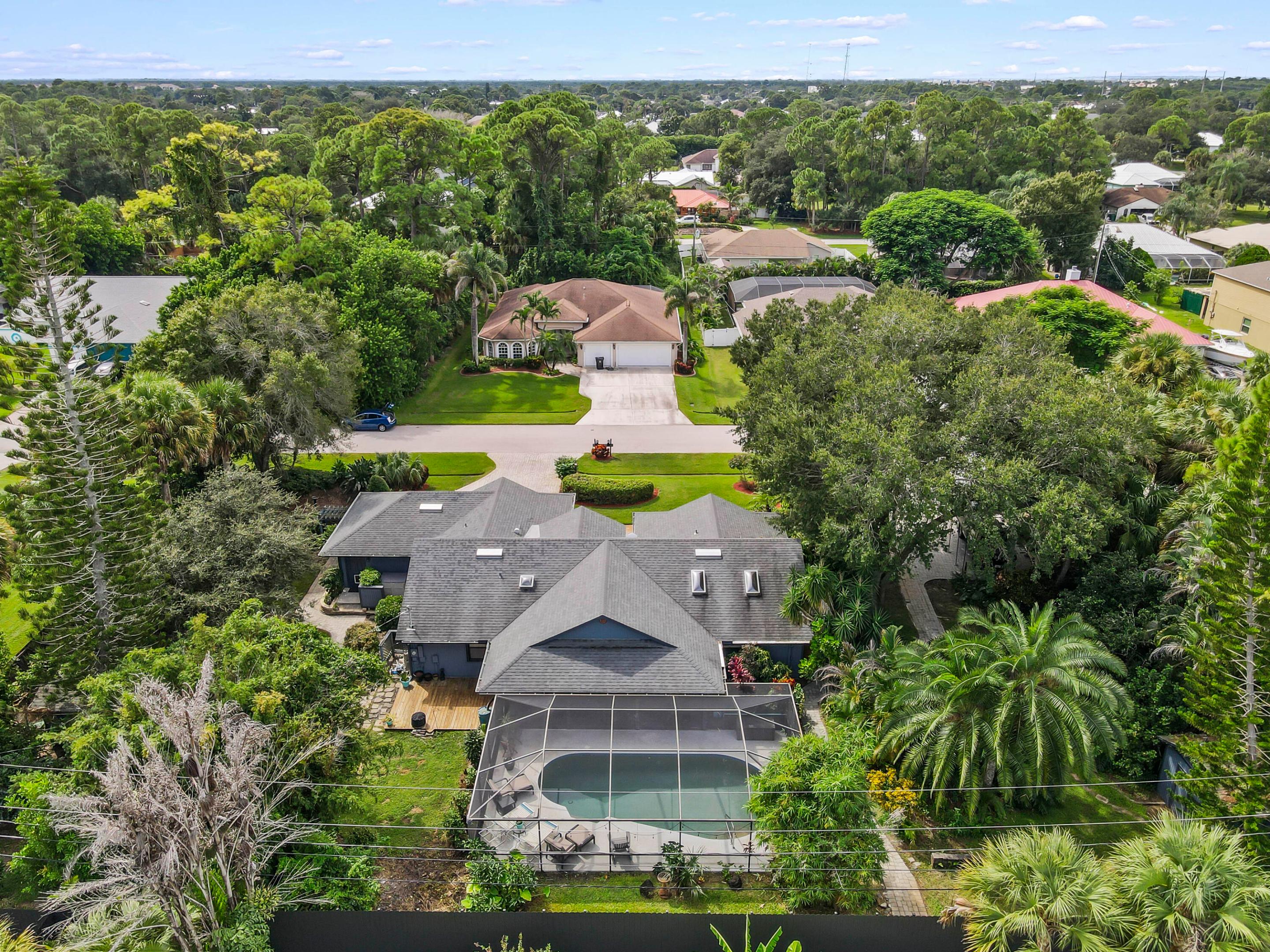 Aerial view of a leafy home and screened swimming pool surrounded by tropical landscaping.