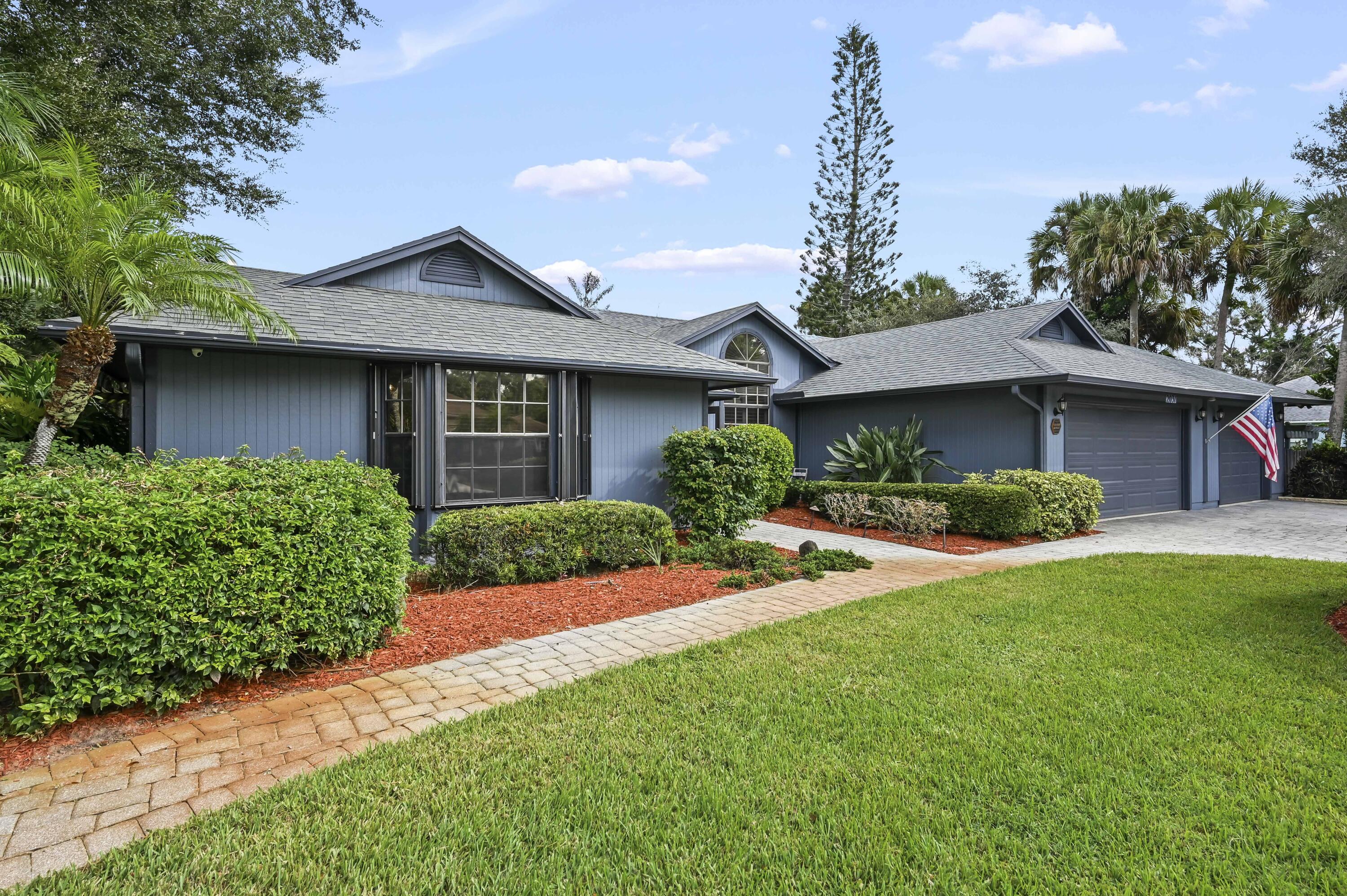 Blue-gray house with a two-car garage, manicured landscaping, and an American flag by the entrance.