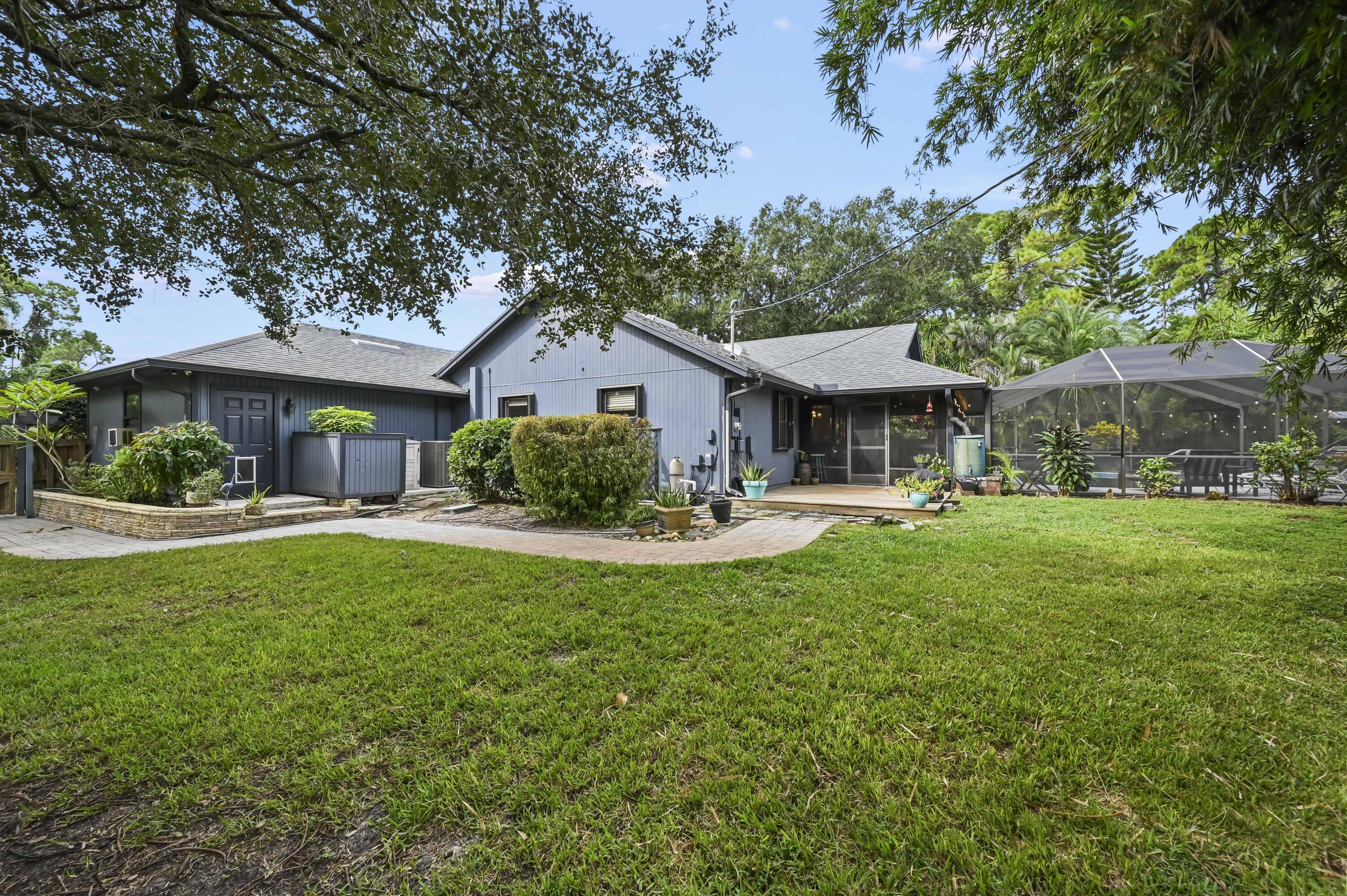 Blue-gray home with a screened pool enclosure, patio, and tree-framed backyard lawn.