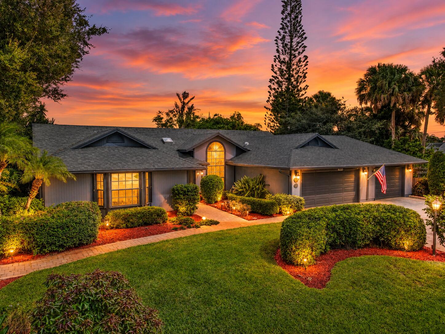 Single-story home with landscaped front yard and glowing arched entry at sunset.
