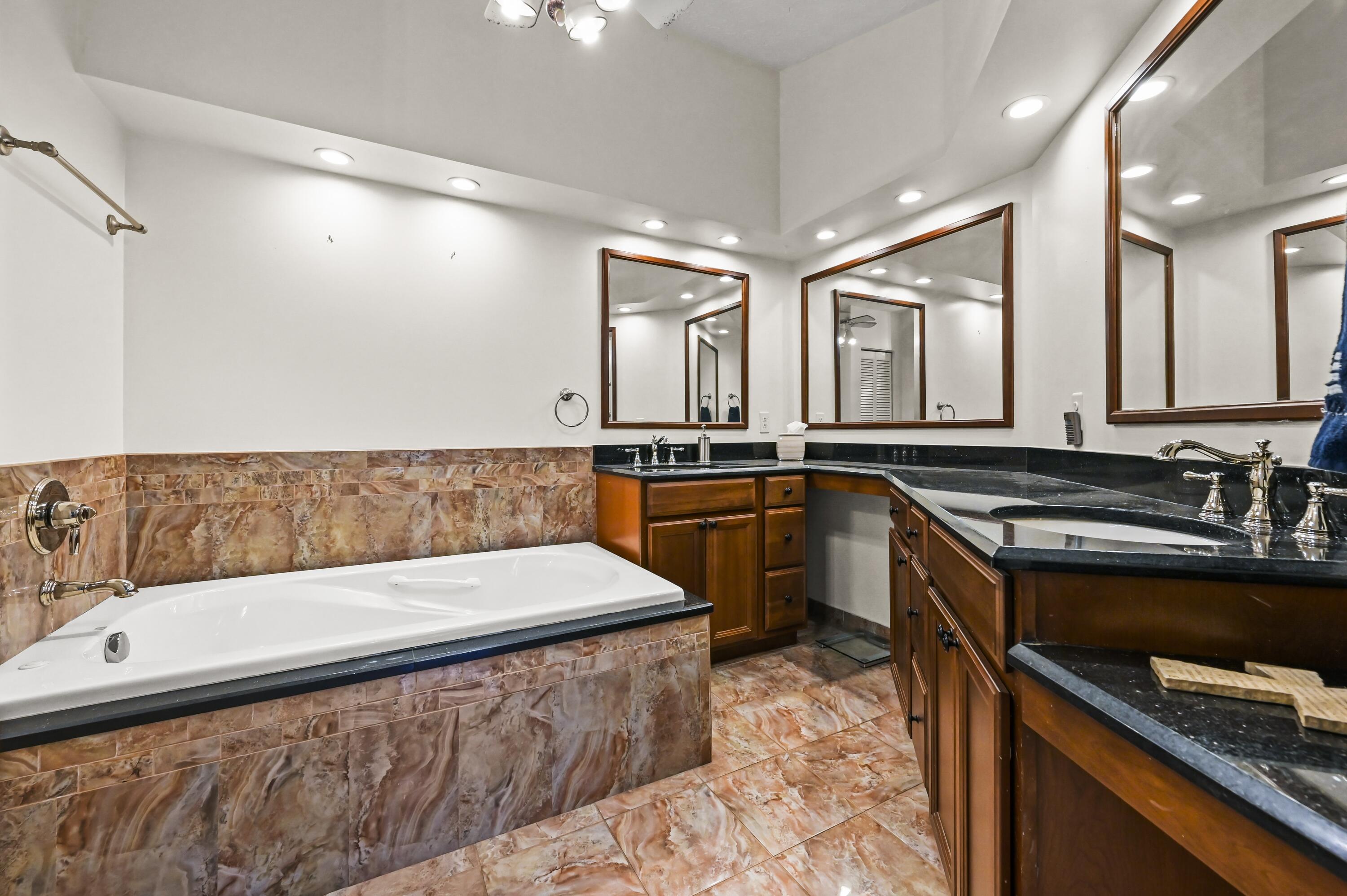Bathroom with a large soaking tub, marble-pattern tile, and dark wood vanities with black counters.