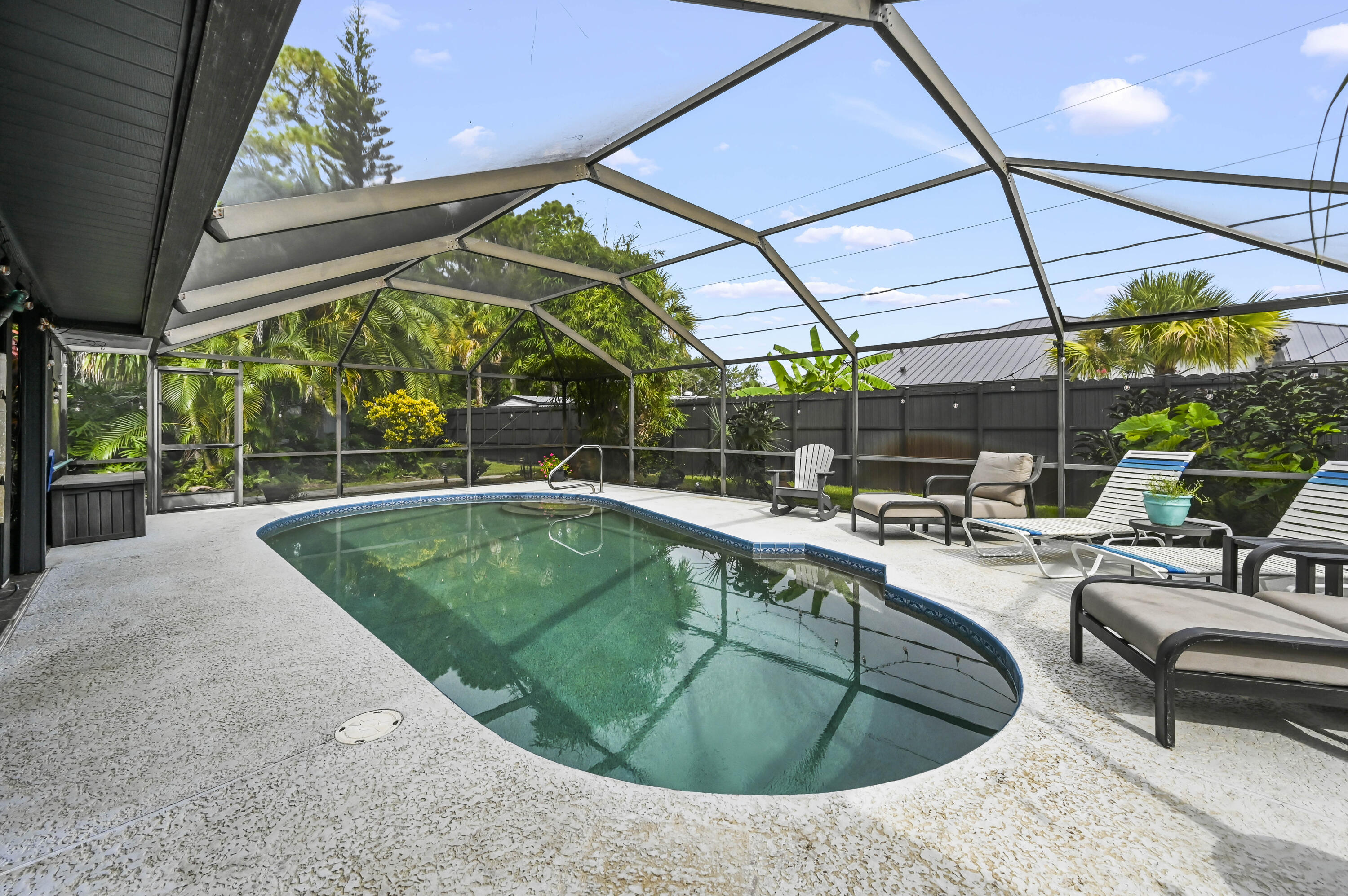 Screened backyard pool with lounge chairs, tropical landscaping, and a bright open view of the sky.