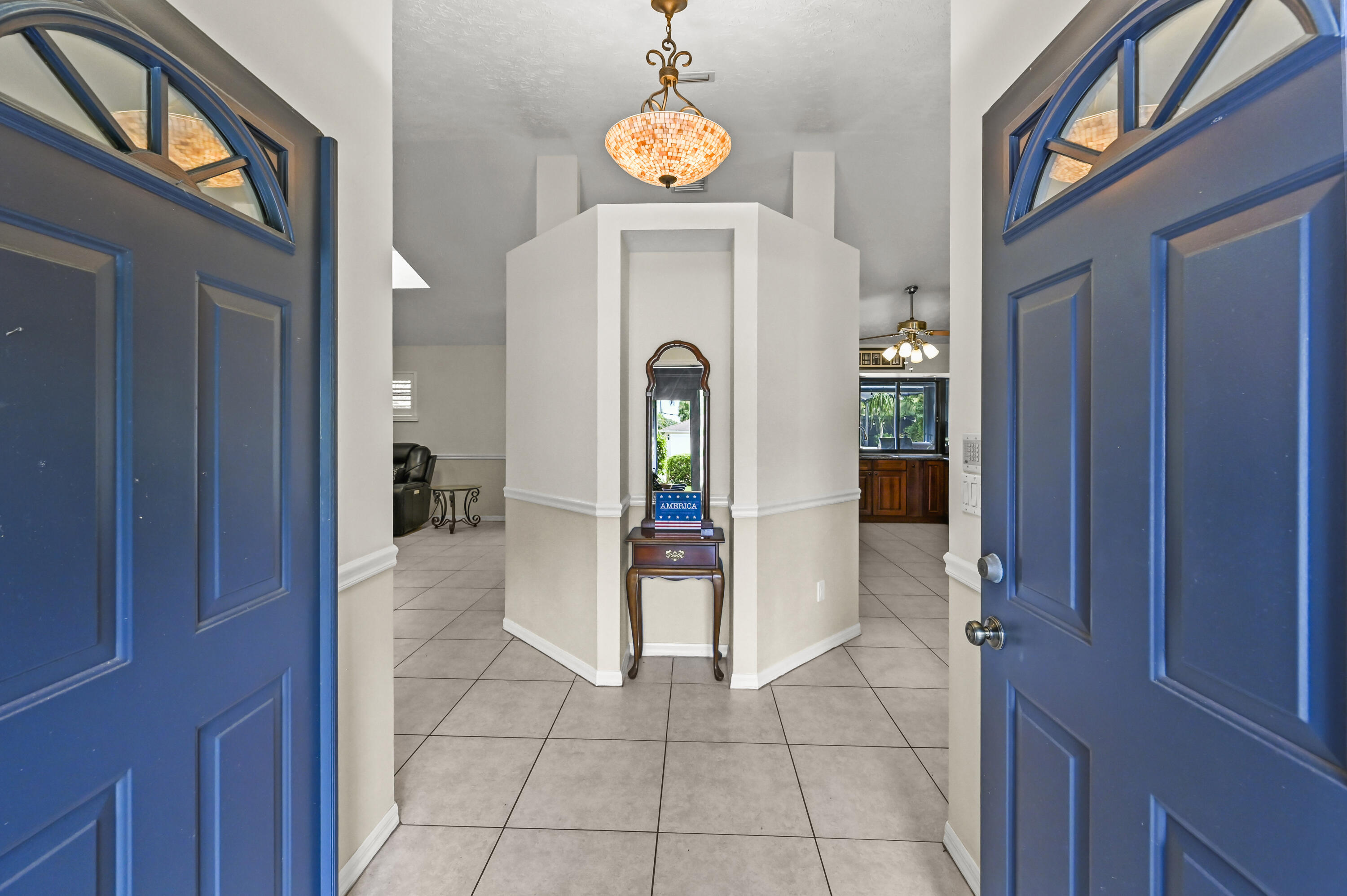 Tiled entry foyer with open blue doors, a wooden console table, and a mosaic pendant light.