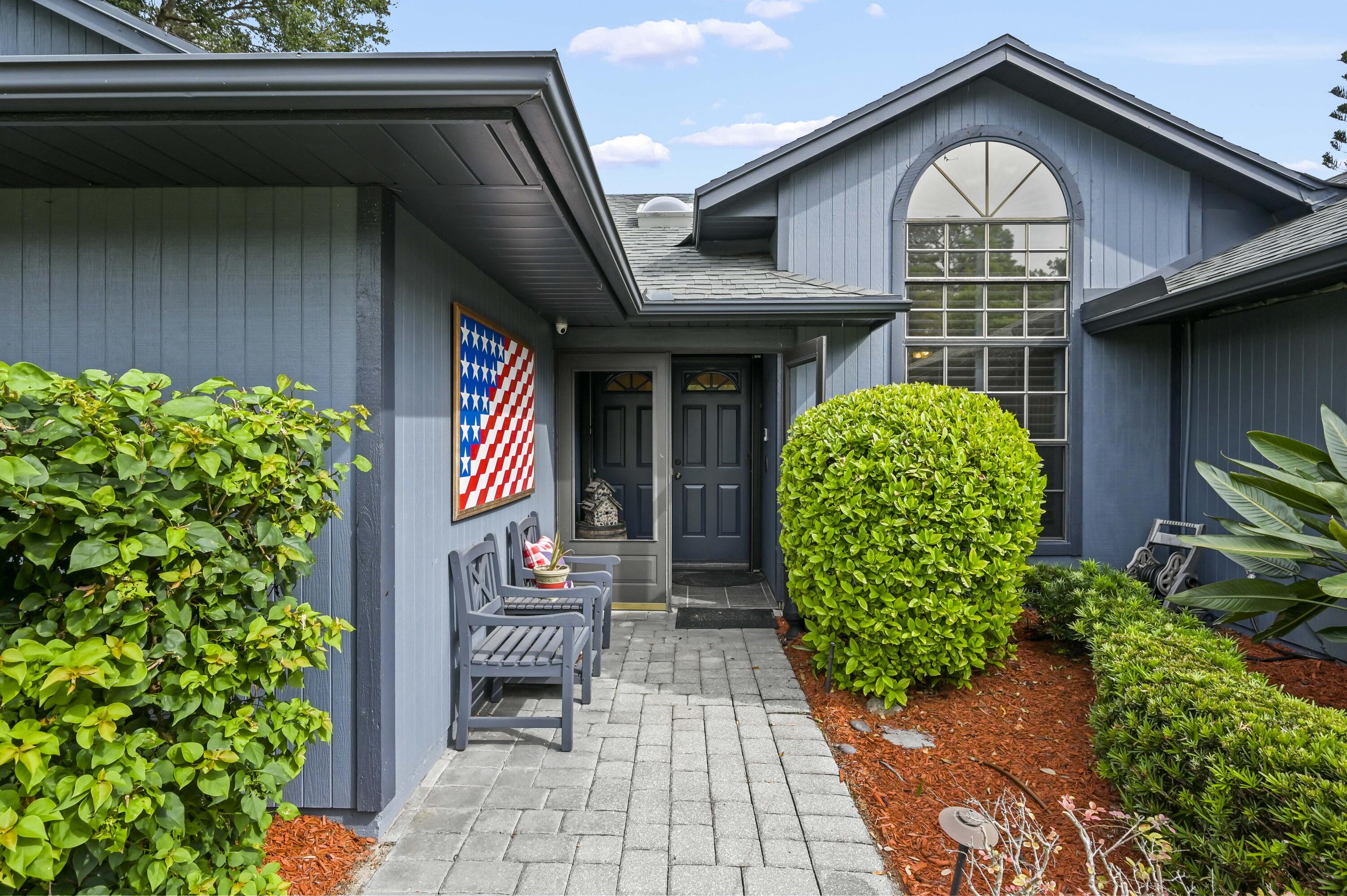 Blue-gray home entrance with an arched window, dark double doors, and a landscaped paved walkway.