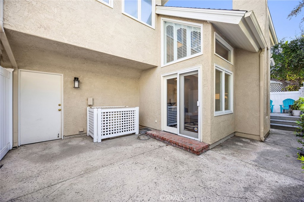 Rear exterior of a stucco home with a concrete patio, sliding glass door, and fenced seating area.