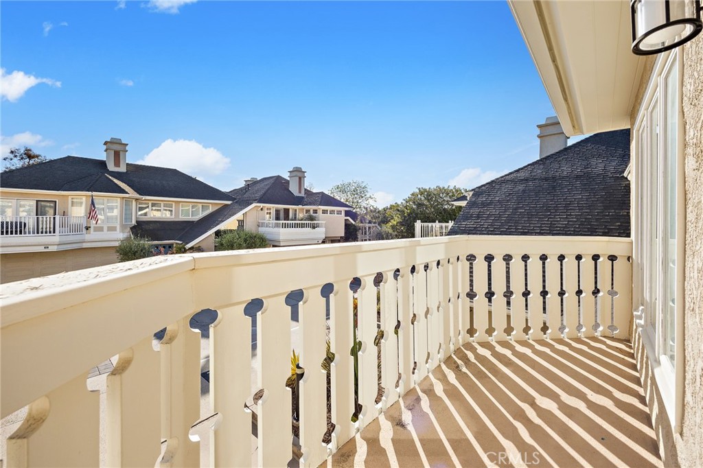 Second-story balcony with cream railing overlooking neighboring homes under a clear blue sky.