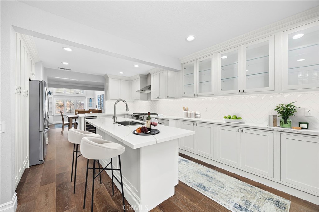 White kitchen with glass-front cabinets, a large island, two stools, and dark wood floors.