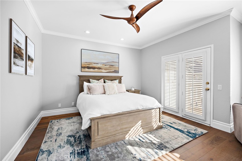 Furnished bedroom with a large bed, white plantation shutters, hardwood floors, and a patterned rug.