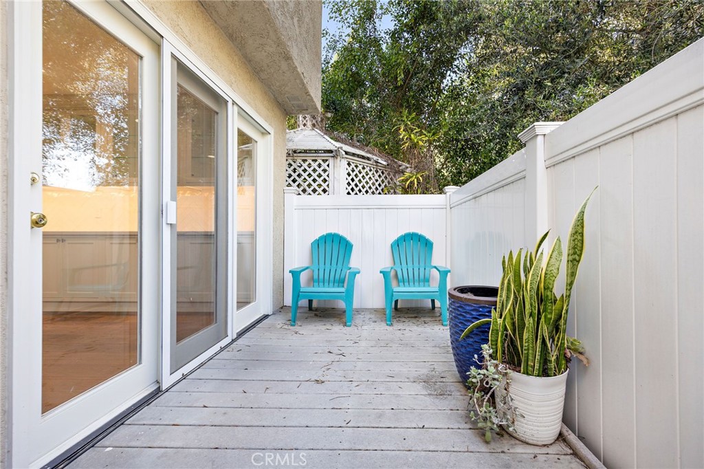 Patio with two turquoise chairs, white fencing, gray decking, and potted plants.