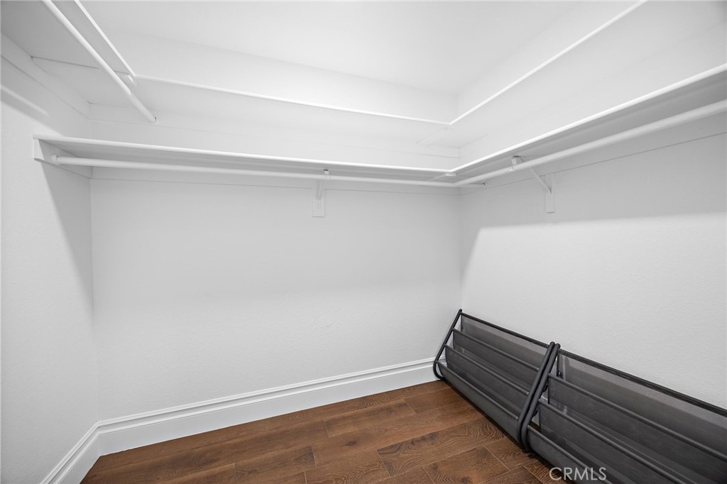 Empty walk-in closet with wraparound hanging rods, upper shelves, and wood-look flooring.