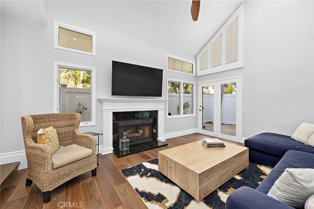 Living room with a fireplace, vaulted ceiling, wicker chair, and glass doors to a fenced patio.